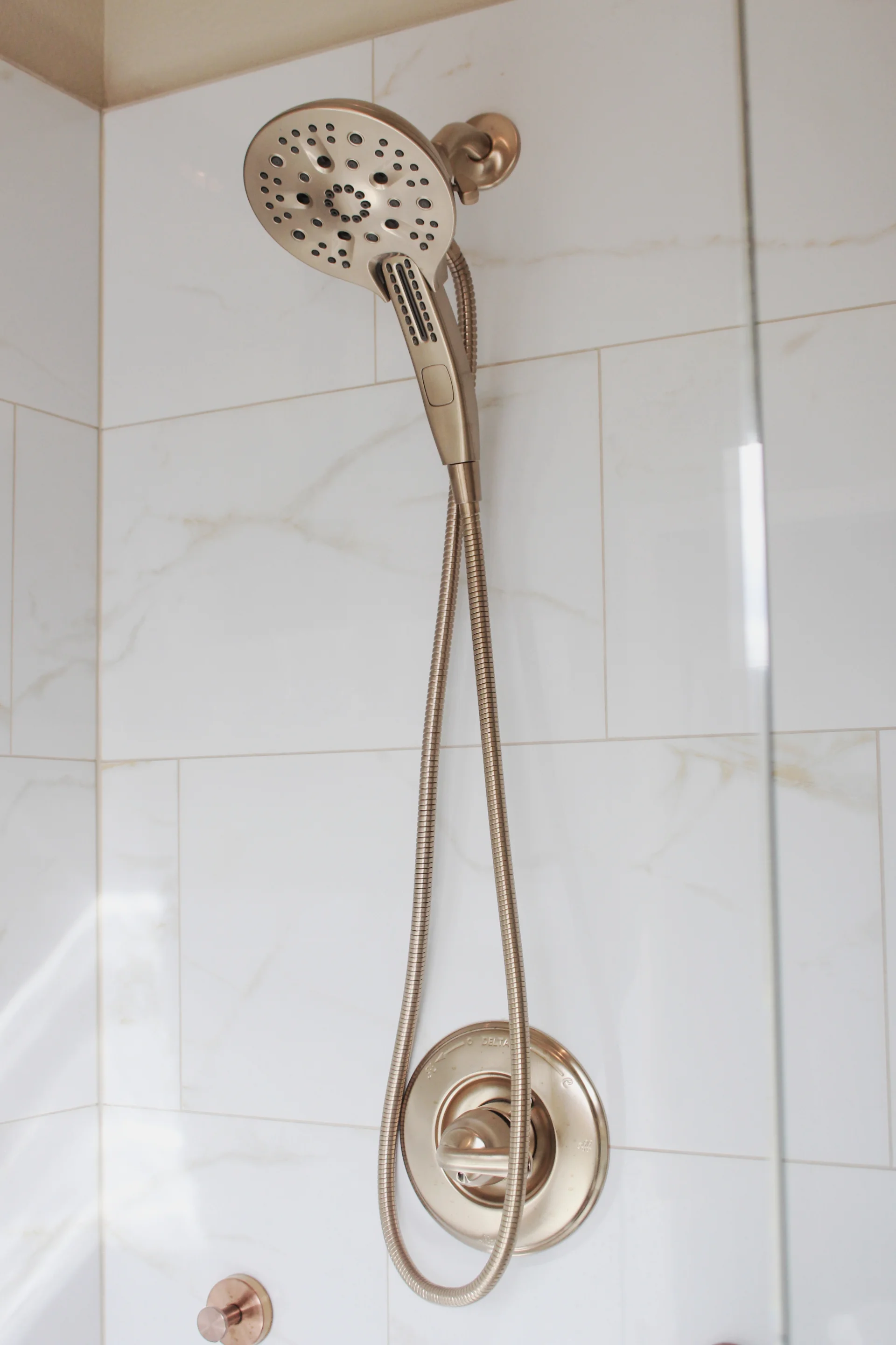 Modern shower with a detachable gold showerhead and hose against glossy white tiled wall, creating a sleek and luxurious bathroom atmosphere.
