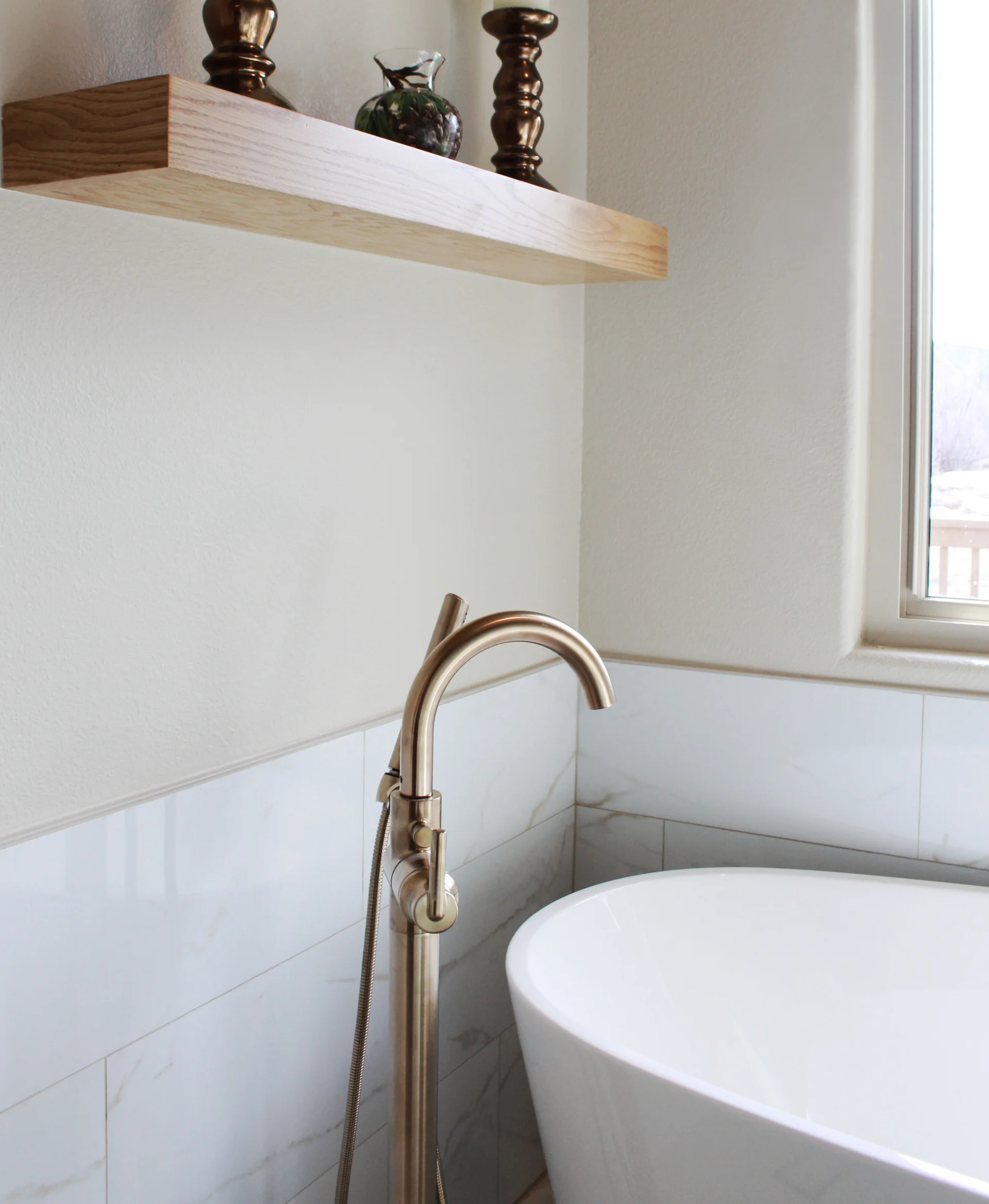 Elegant bathroom scene with a modern curved faucet beside a white bathtub. A wooden shelf with decorative items is mounted on a light-colored wall.