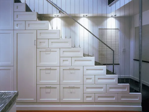 A white stair case with abstract shelving for storage built in underneath the stairs