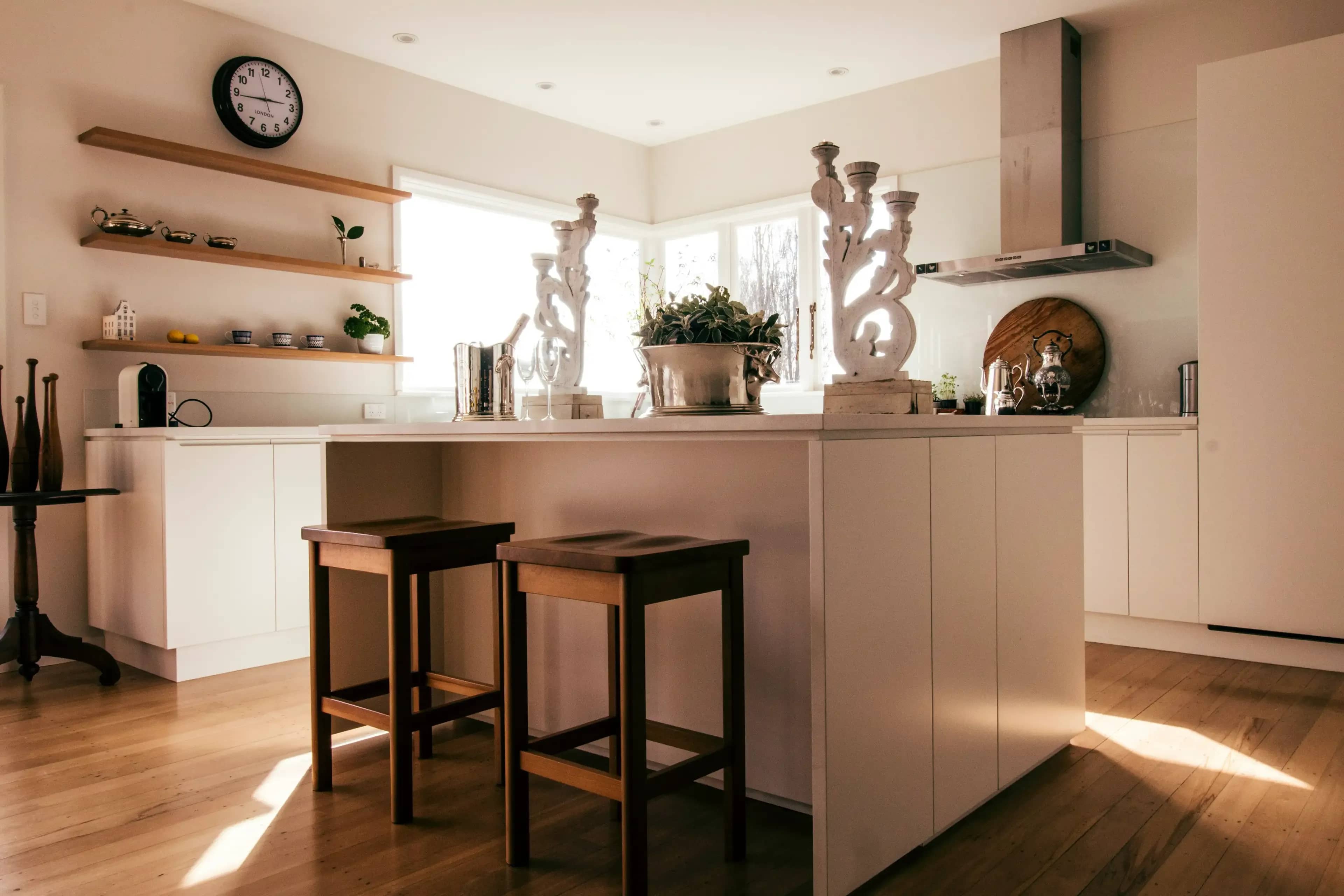 A photograph of a new kitchen remodel with a modern / minimal feel, square stools, white cabinets, a spacious center island and wooden shelves with white countertops