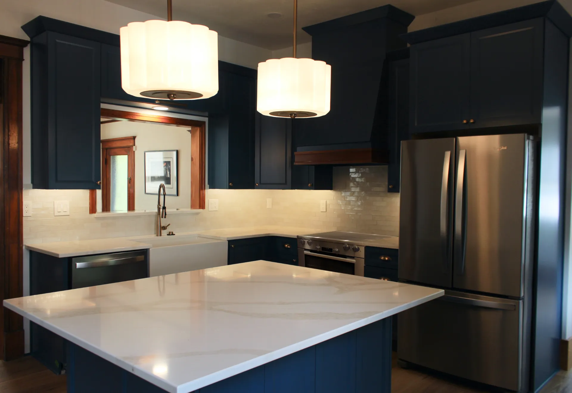 A modern kitchen with dark blue cabinets, stainless steel appliances, and a white island. Two large, white pendant lights hang above, creating a sleek and cozy ambiance.