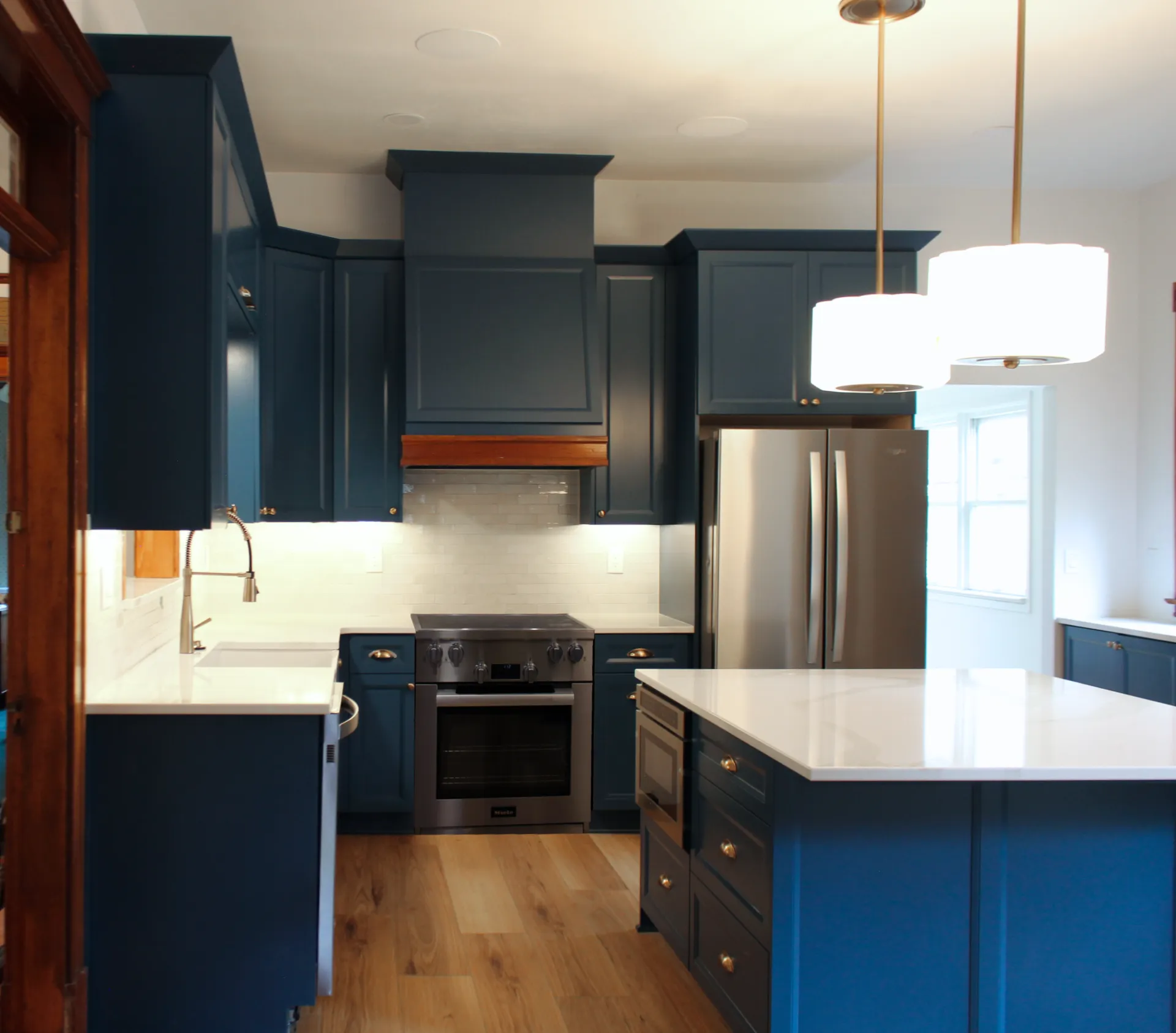Modern kitchen with navy cabinets, white countertops, and stainless steel appliances. Light wood flooring and pendant lights create a cozy atmosphere.