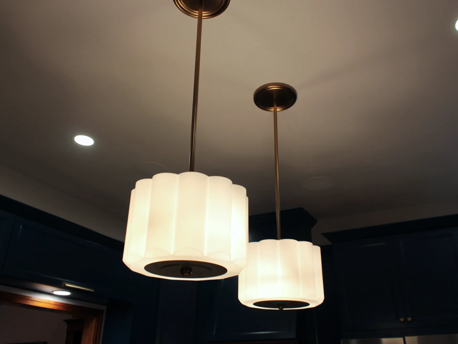 Two elegant pendant lights with white, fluted shades hang from the ceiling, casting a warm glow. The room has a modern, sleek design with dark cabinetry.