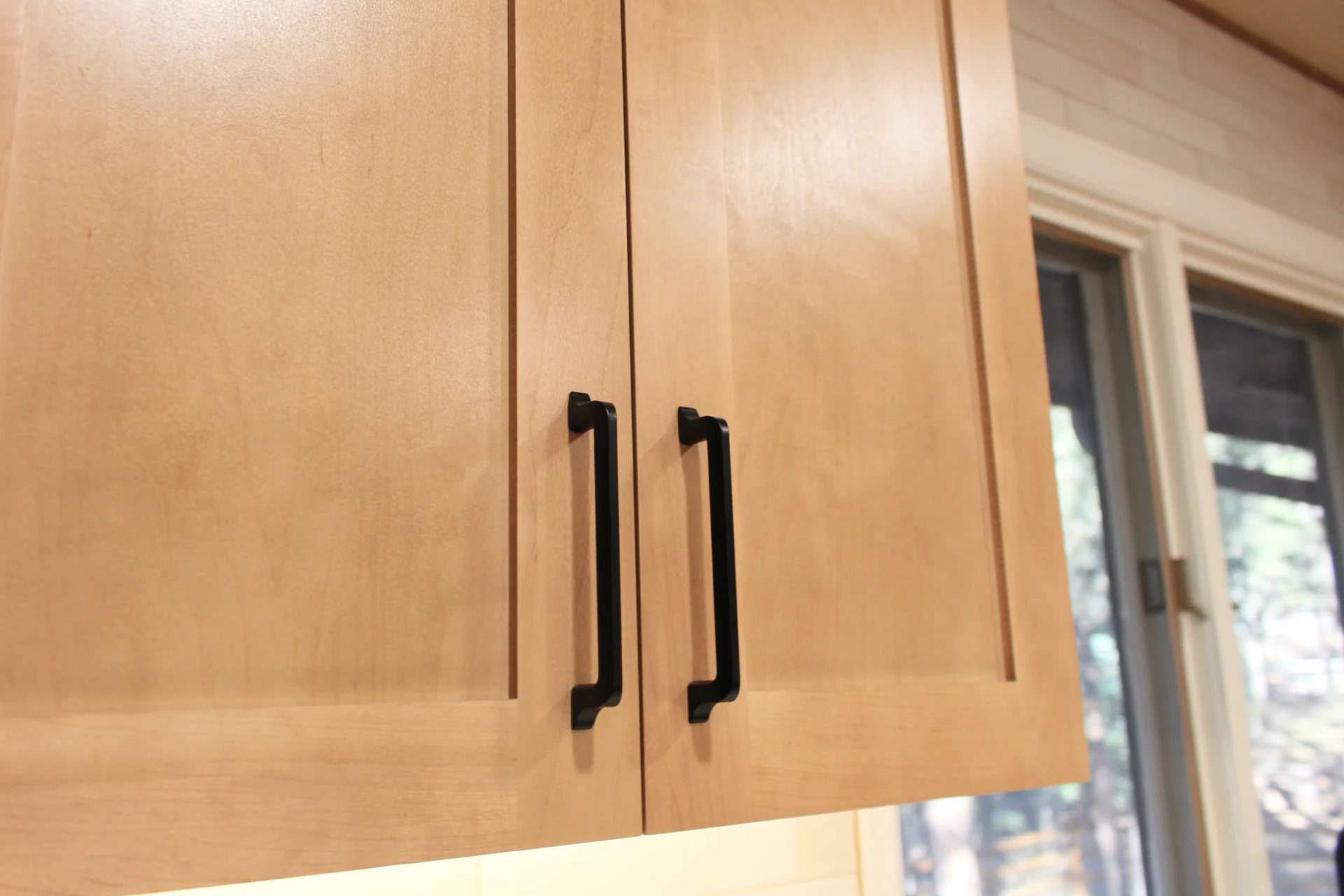 Close-up of natural wood kitchen cabinet doors with sleek black handles. Soft light highlights the wood grain, creating a warm and modern ambiance.