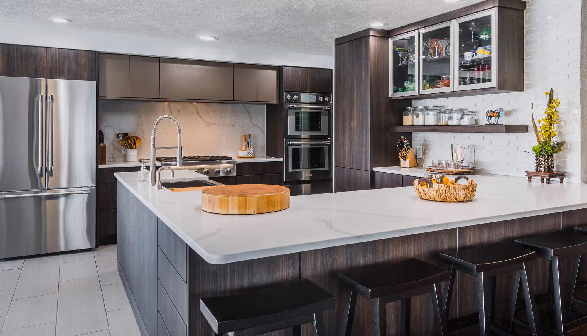 Modern kitchen with dark wood cabinetry, stainless steel appliances, white marble countertops, and a large kitchen island with black stools.