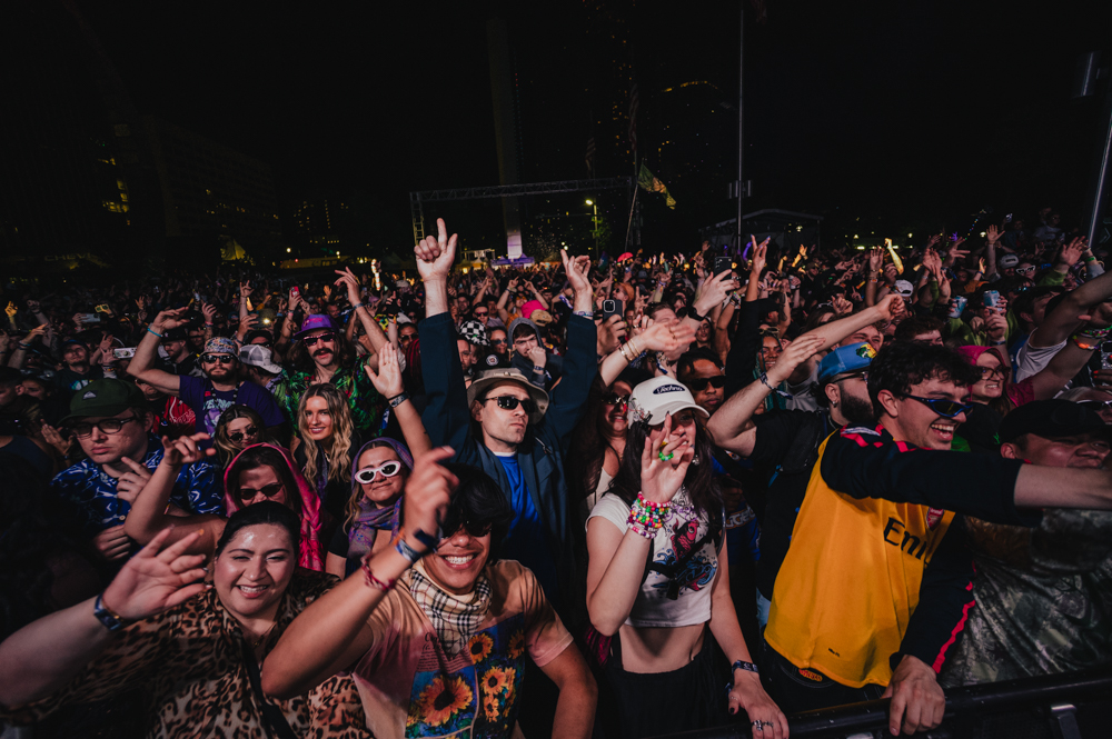 Crowd of happy people dancing and raising their hands at a lively outdoor nighttime concert.
