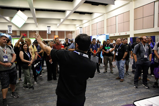 Presenter leading a packed demo at an edtech conference expo, engaging K-12 educators around a booth during the trade show.