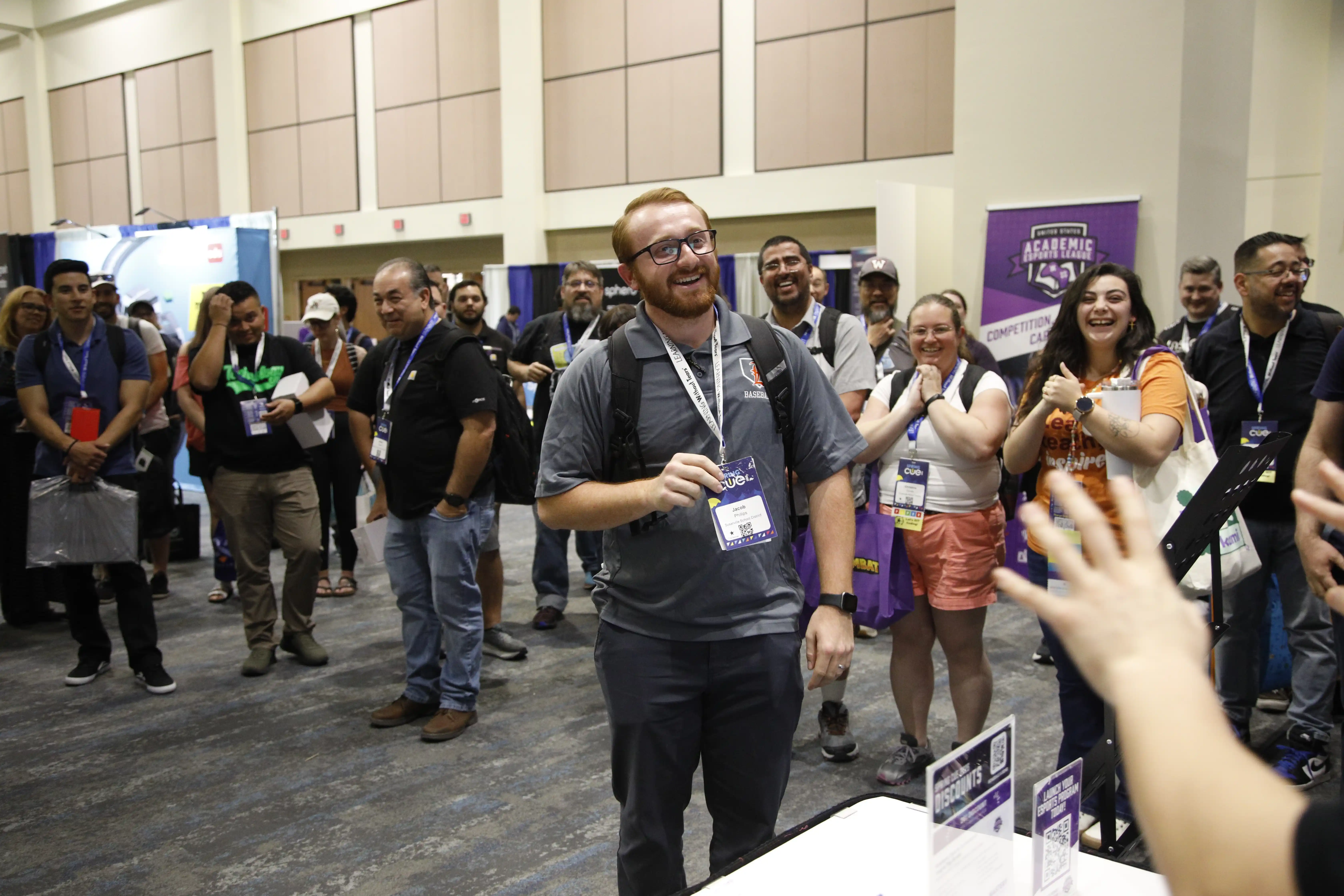 Crowd of educators cheers as a raffle winner is announced at the Spring CUE STEM Zone, with US Academic Esports League signage visible in the background.