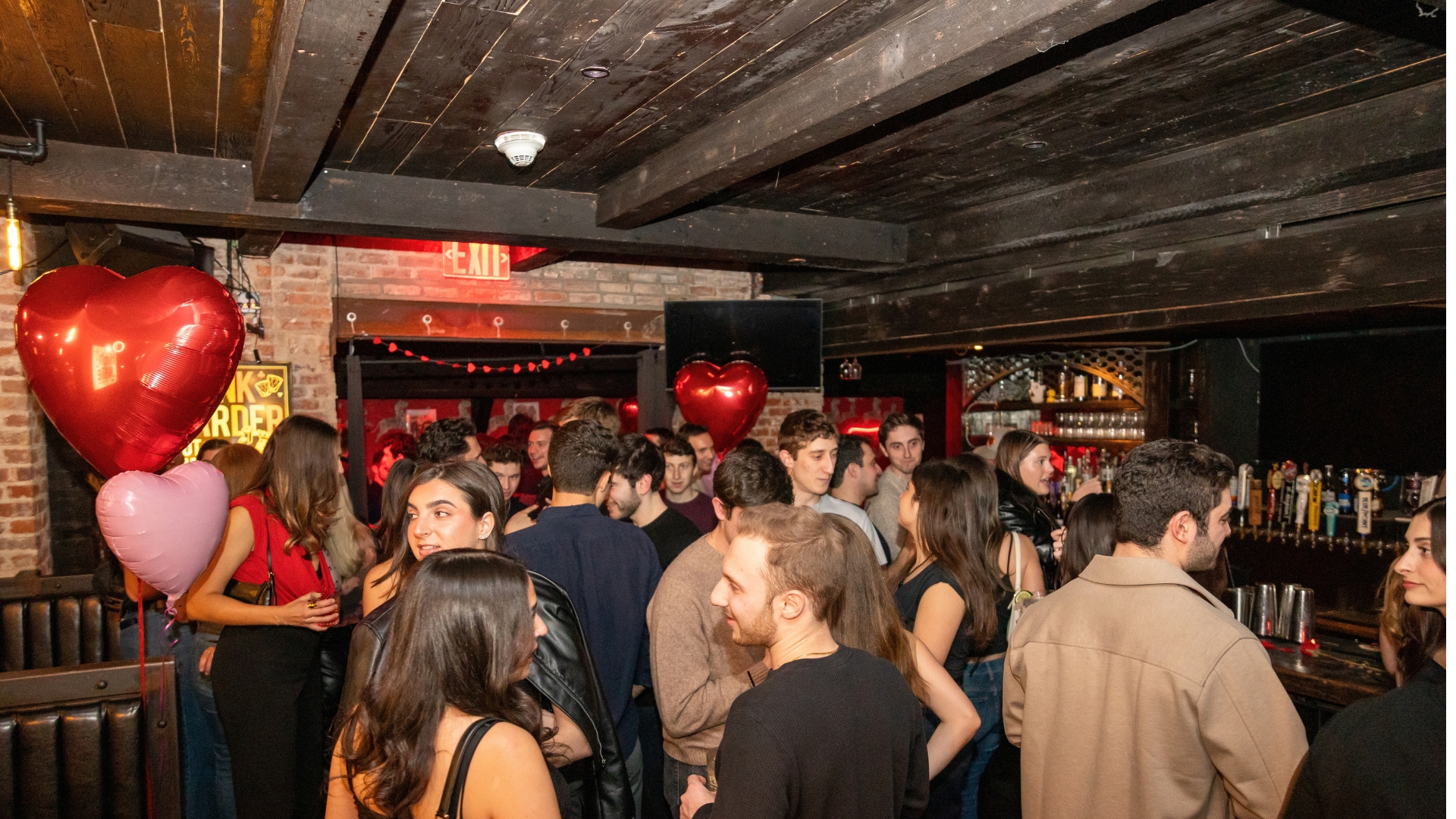 A crowded How Jew Meet party with red heart balloons