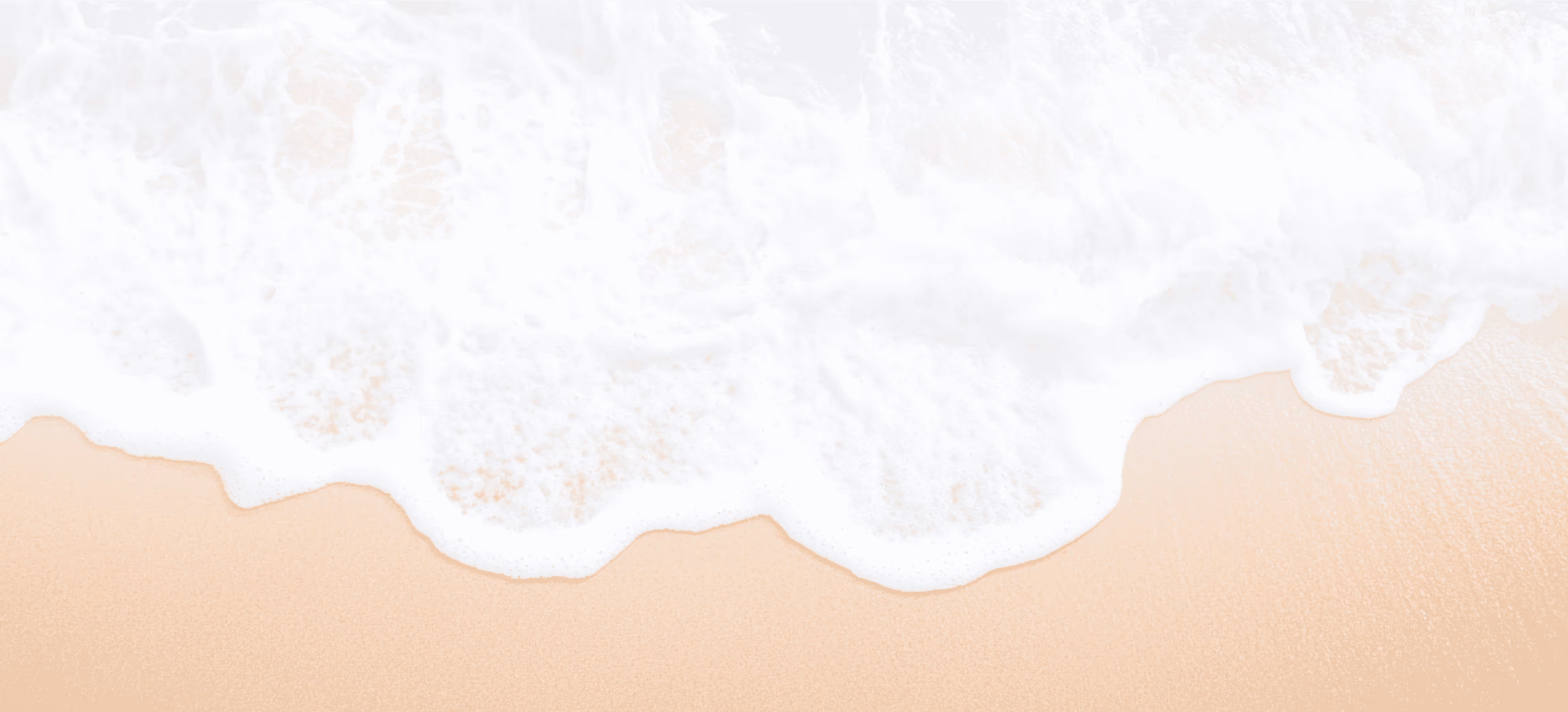 White ocean waves gently washing onto soft beige sandy beach.