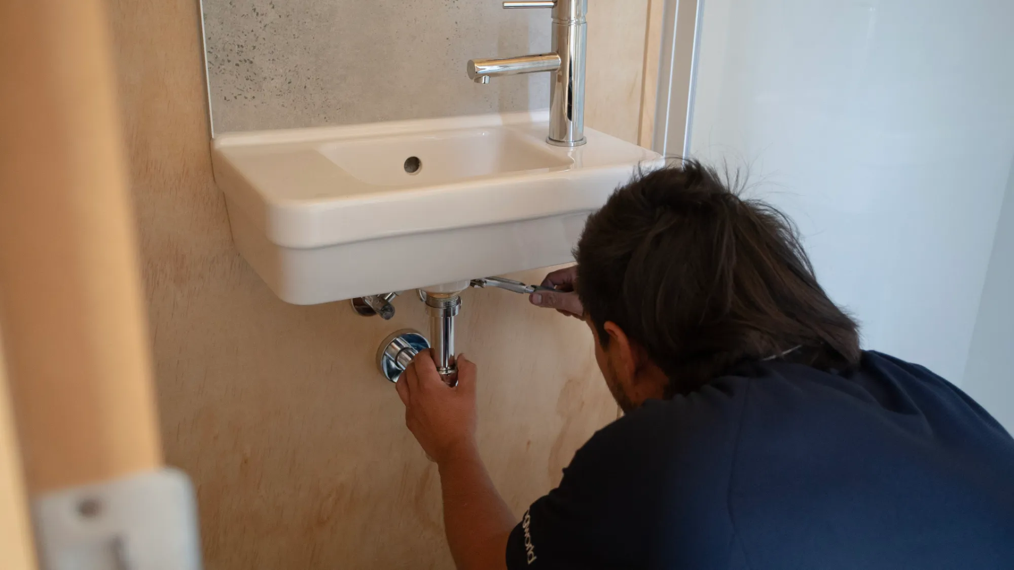 Plumber fitting the waste pipe under a wall-hung bathroom basin