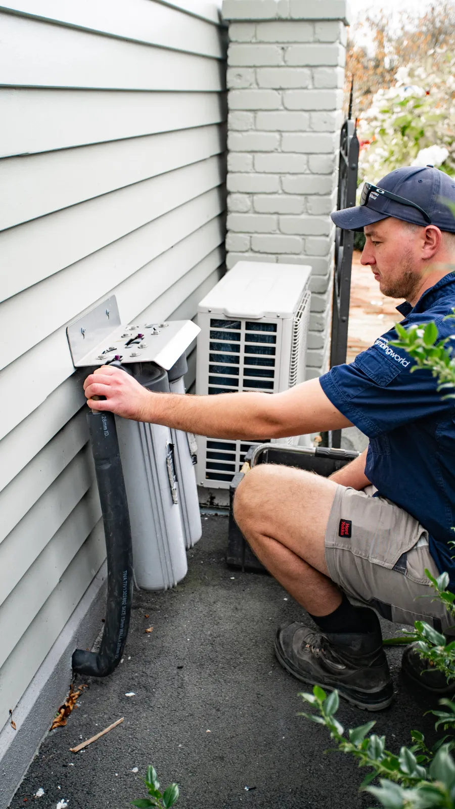Plumber installing a whole-house water filter on the side of a home