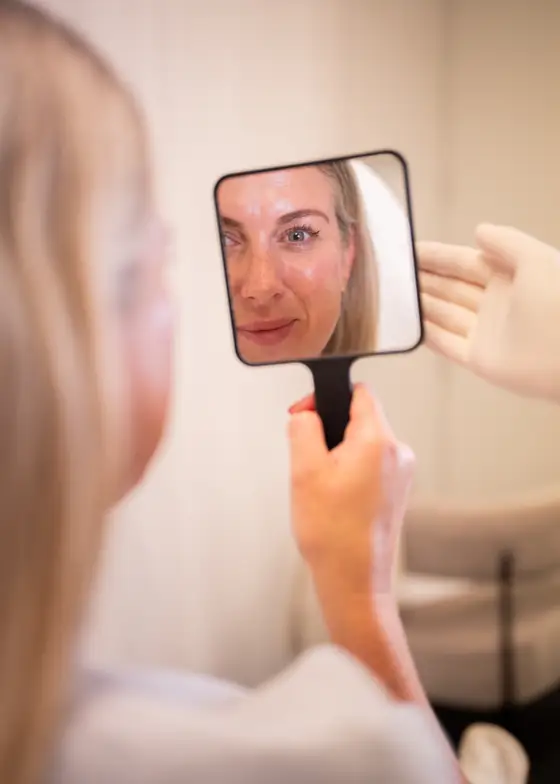 Client checking her results in a hand mirror after treatment at Andrea Harris Aesthetics
