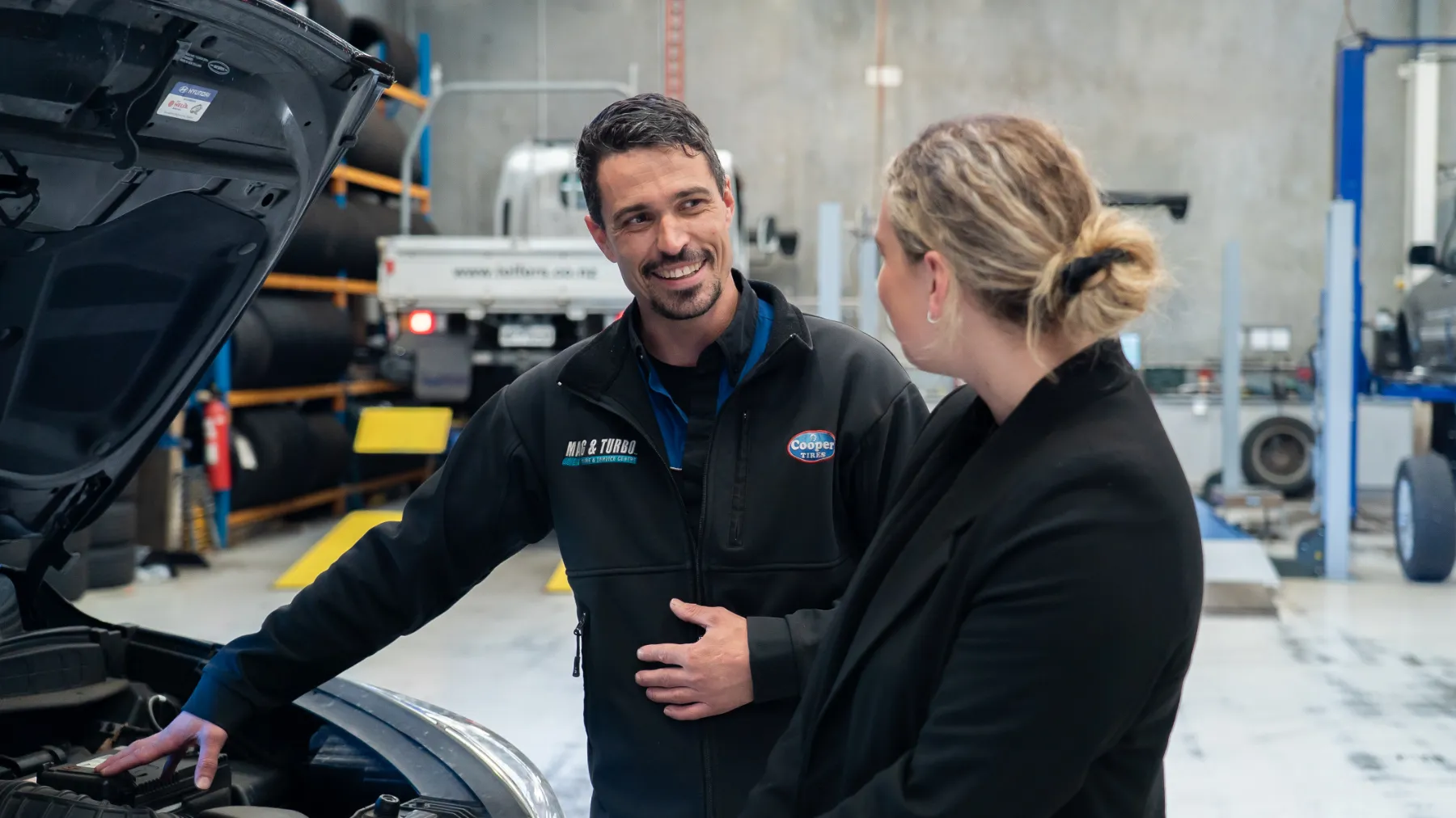 Mag & Turbo technician talking with a customer beside a car in the workshop