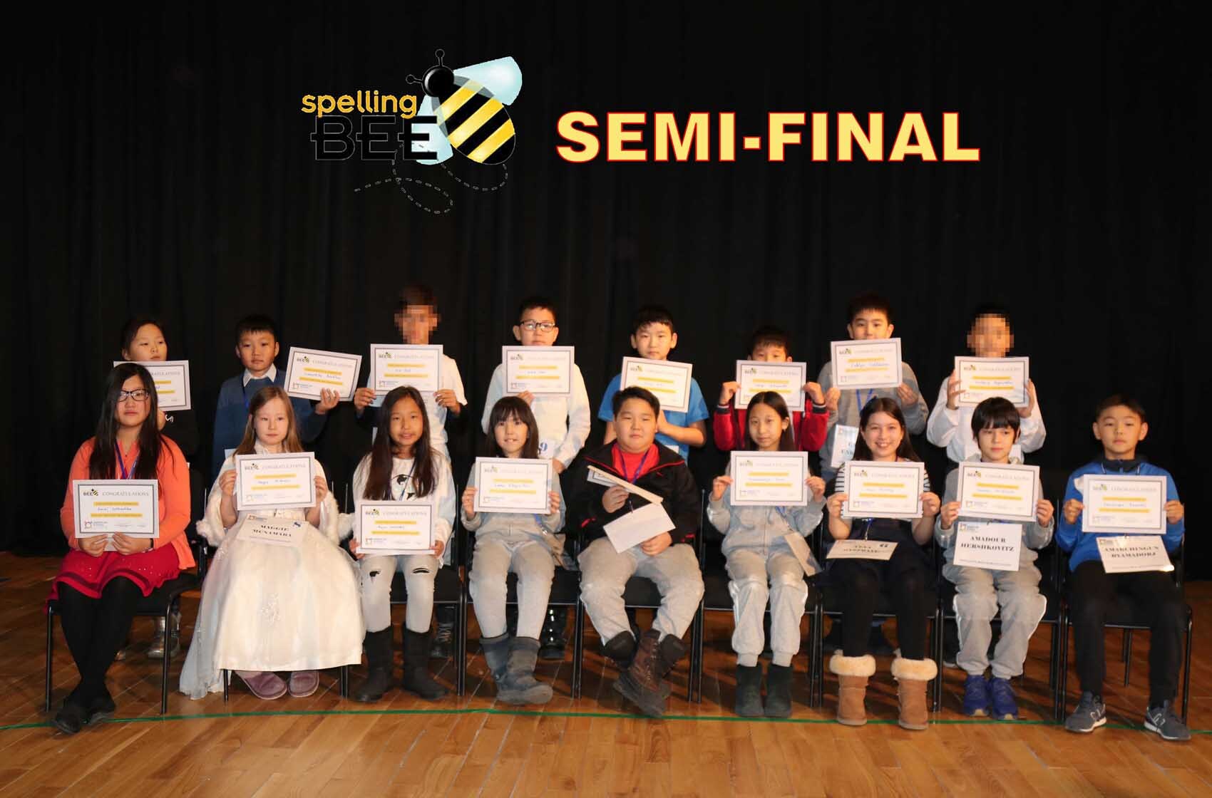 Group of children sitting and standing on a stage holding certificates under a banner that reads 'Spelling Bee Semi-Final'.