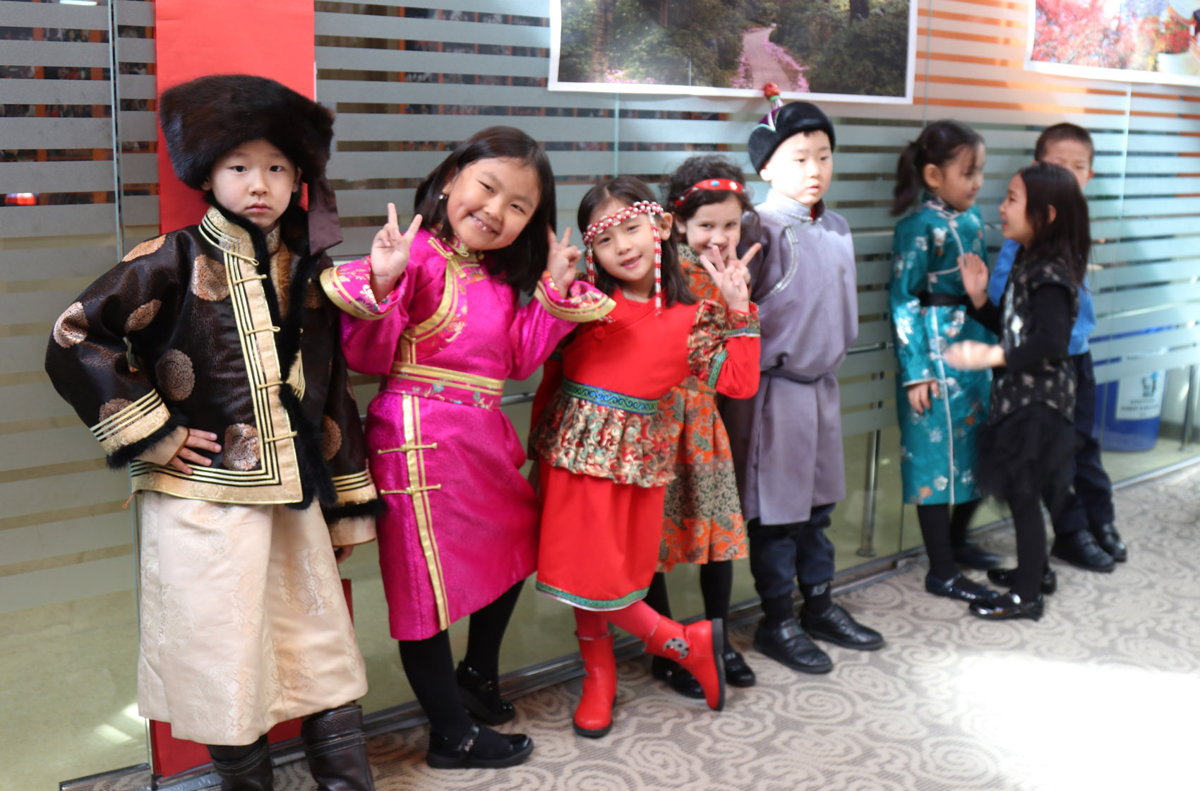 Group of children dressed in colorful traditional costumes posing indoors, with some making peace signs.