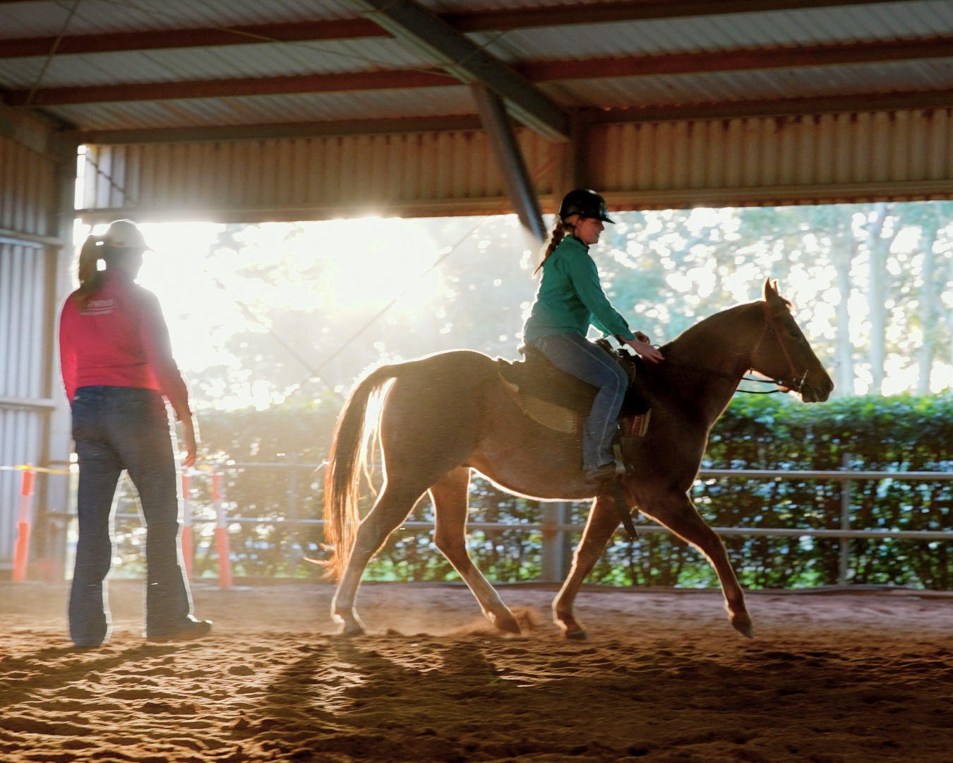 Person riding a horse indoors with another person standing nearby watching.