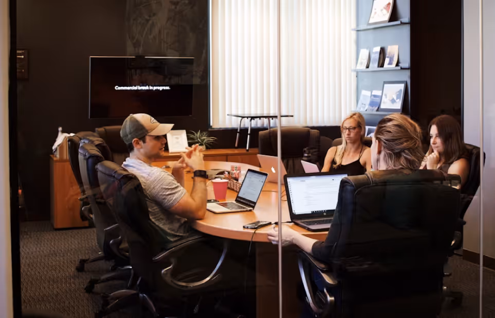 Four people sitting around a conference table with laptops in a modern office meeting room.