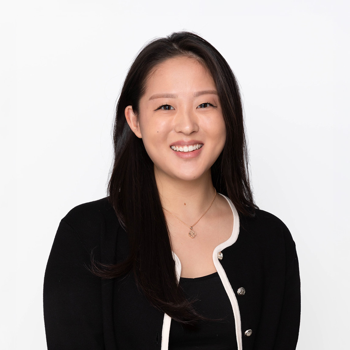 Smiling woman with long black hair wearing a black buttoned cardigan and gold pendant necklace.