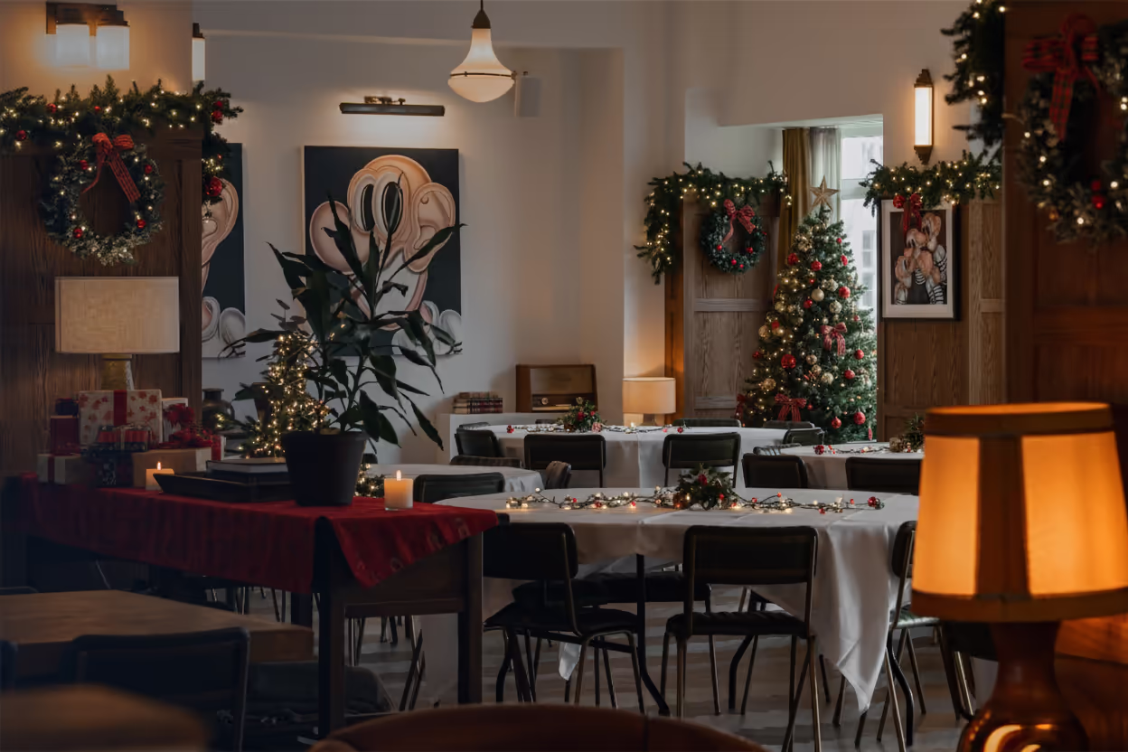 Cozy room decorated for Christmas with a tree, wreaths, candles, and tables with white tablecloths and festive lights.