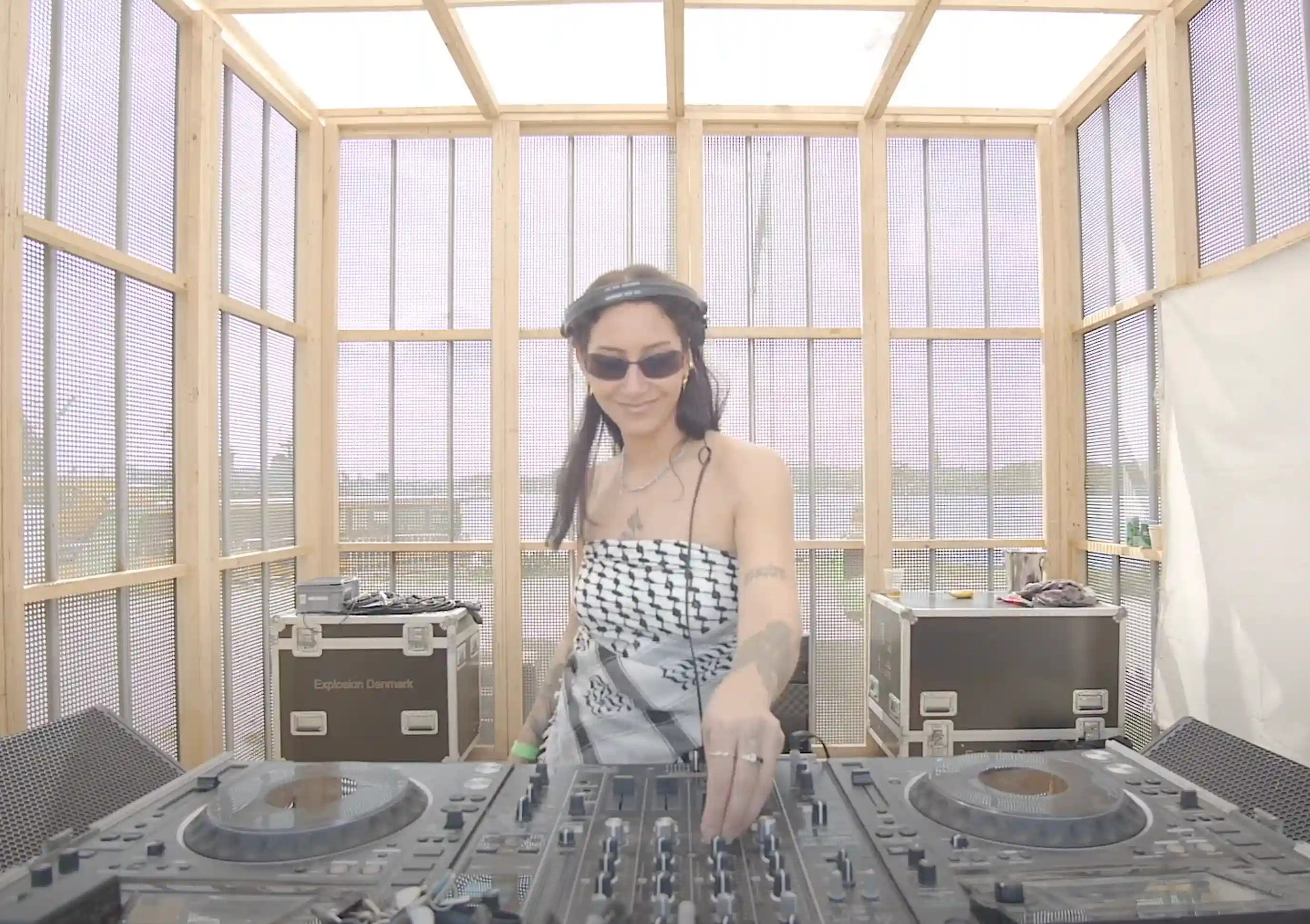 DJ Tjiquita performing a DJ set at Drift Radio during O Days Festival on August 3, 2024 — standing behind the decks, wearing headphones, focused on the mixer, with colorful stage lights and the crowd visible in the background.