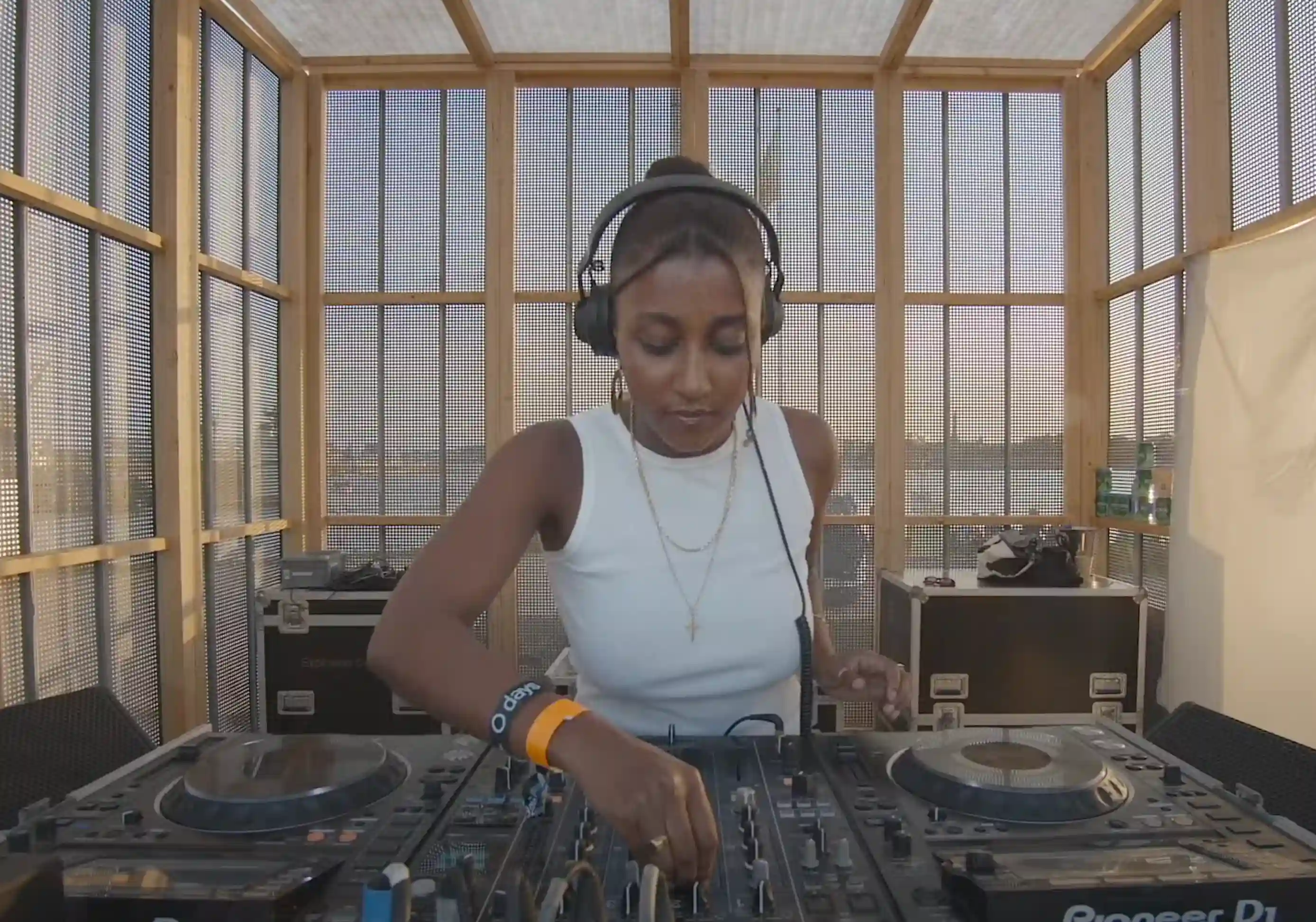 Ruth Belai performing a DJ set at Drift Radio during O Days Festival on August 1, 2024 — focused on the mixing console, wearing headphones, with colorful stage lights and the audience visible in the background.