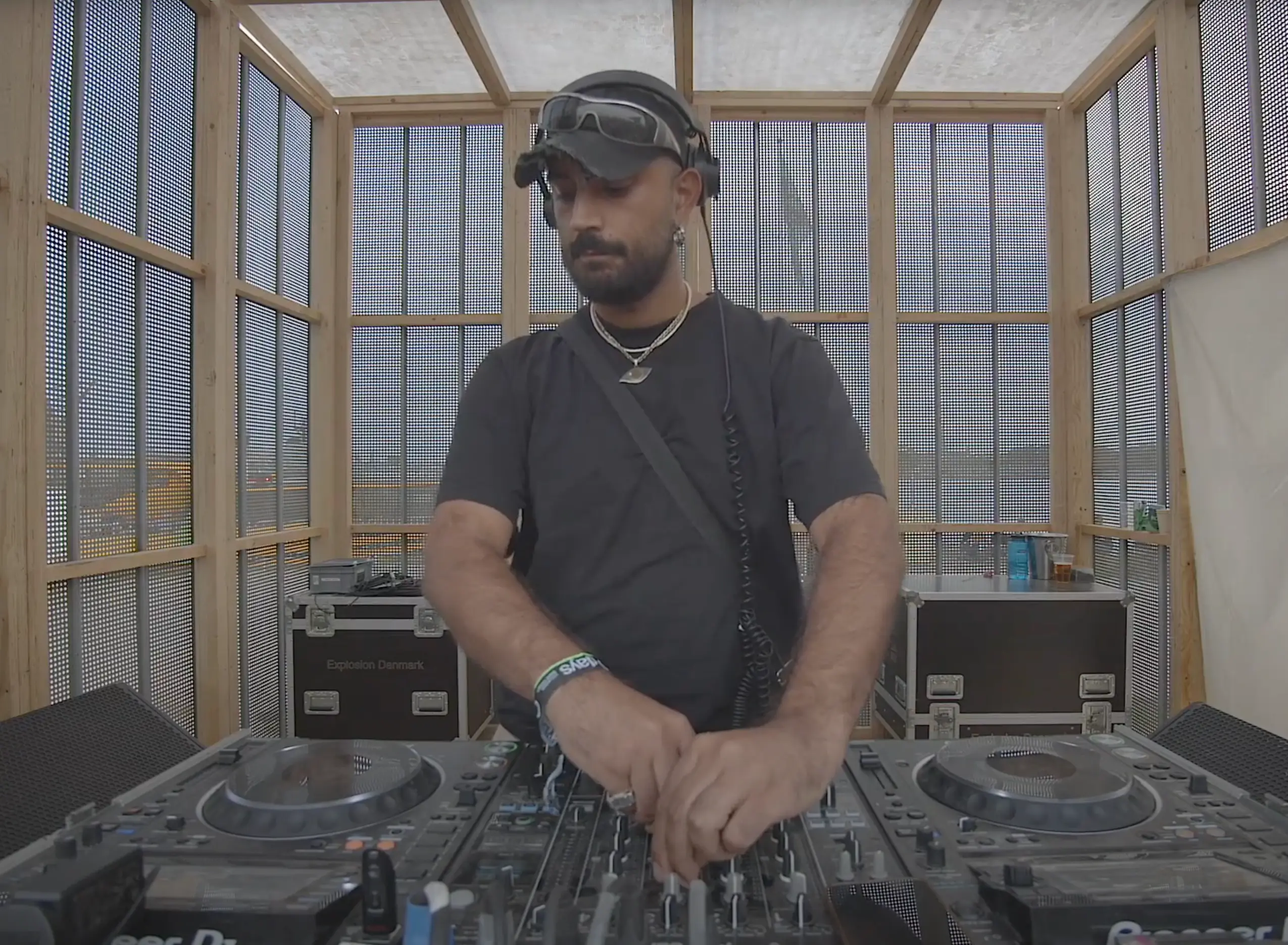 DJ NAH CARE behind the decks at Drift Radio’s O Days Festival set on August 3, 2024 — wearing a cap and headphones, smiling as he mixes hard house and Latin-inspired techno under warm stage lighting.