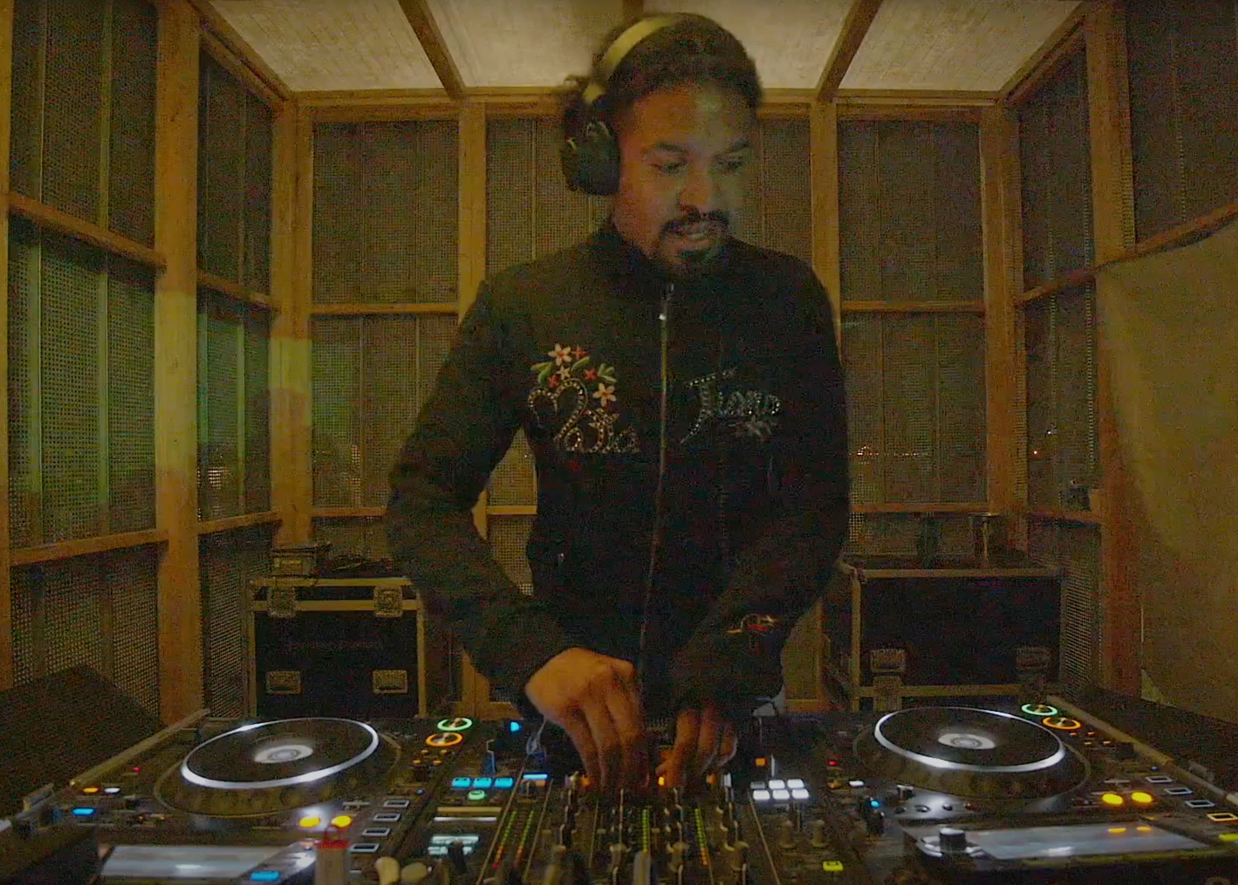 Suzie The Cockroach performing a DJ set at Drift Radio during O Days Festival on August 3, 2024 — focused on the mixing console, wearing headphones, with colorful stage lights and the crowd faintly visible in the background.