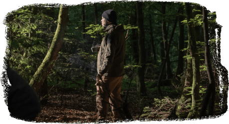 Ein Mann in Outdoor-Bekleidung steht im Wald und blickt in die Ferne.