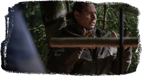 Mann in Outdoor-Bekleidung erklärt mit Gesten in einem Wald.