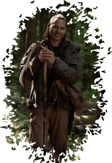 Person mit langem Haar, die in einem Wald steht und mit beiden Händen eine große Astgabel hält.