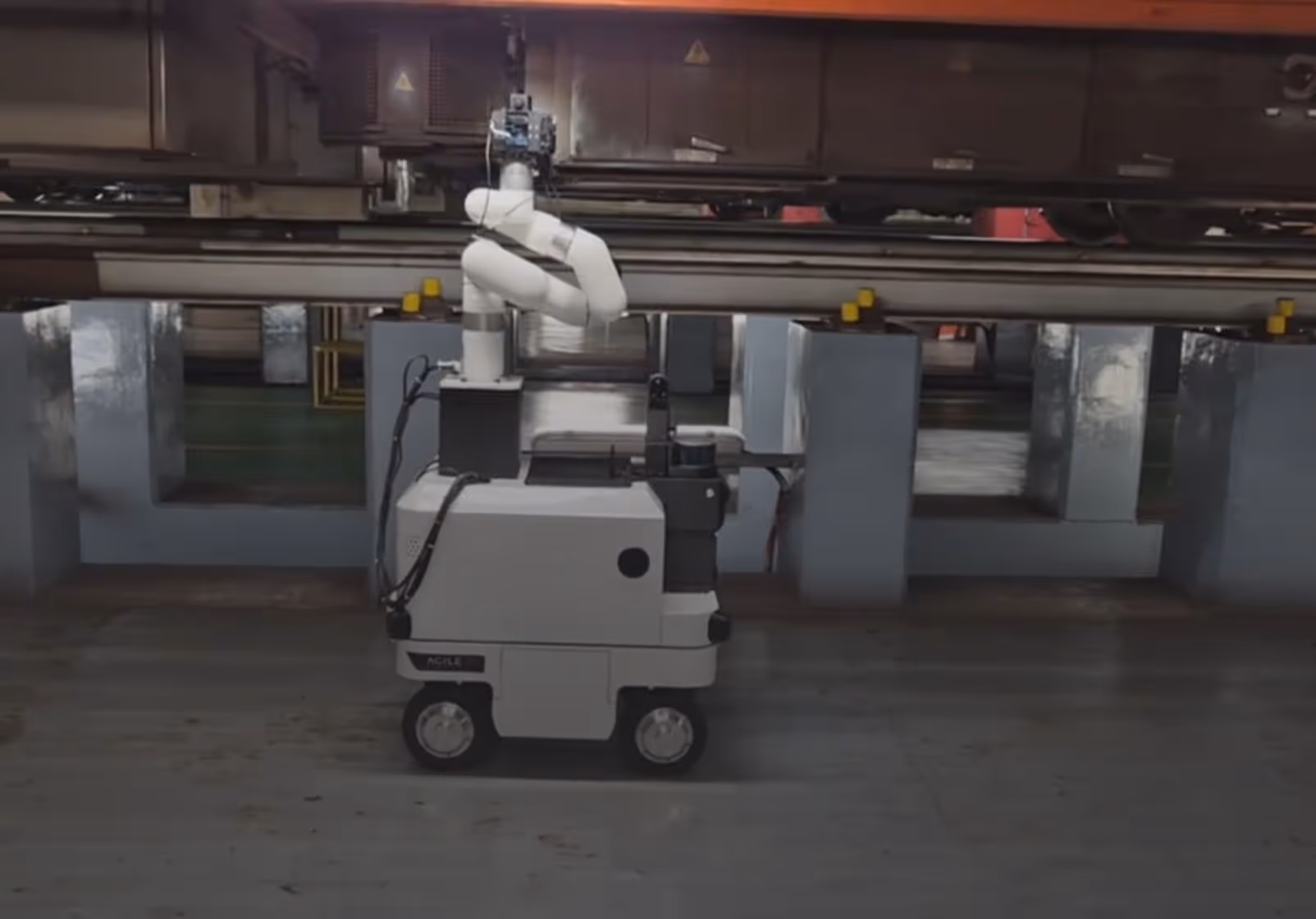 Compact white robotic arm mounted on a mobile wheeled base inside an industrial setting.