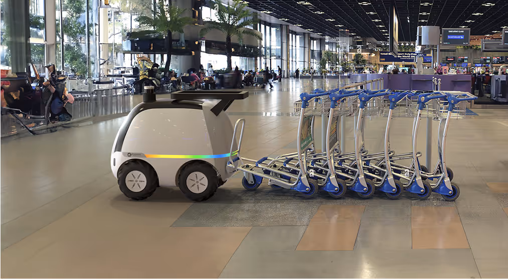 Dasher: Autonomous robot pulling a row of luggage carts inside a spacious, modern airport terminal.