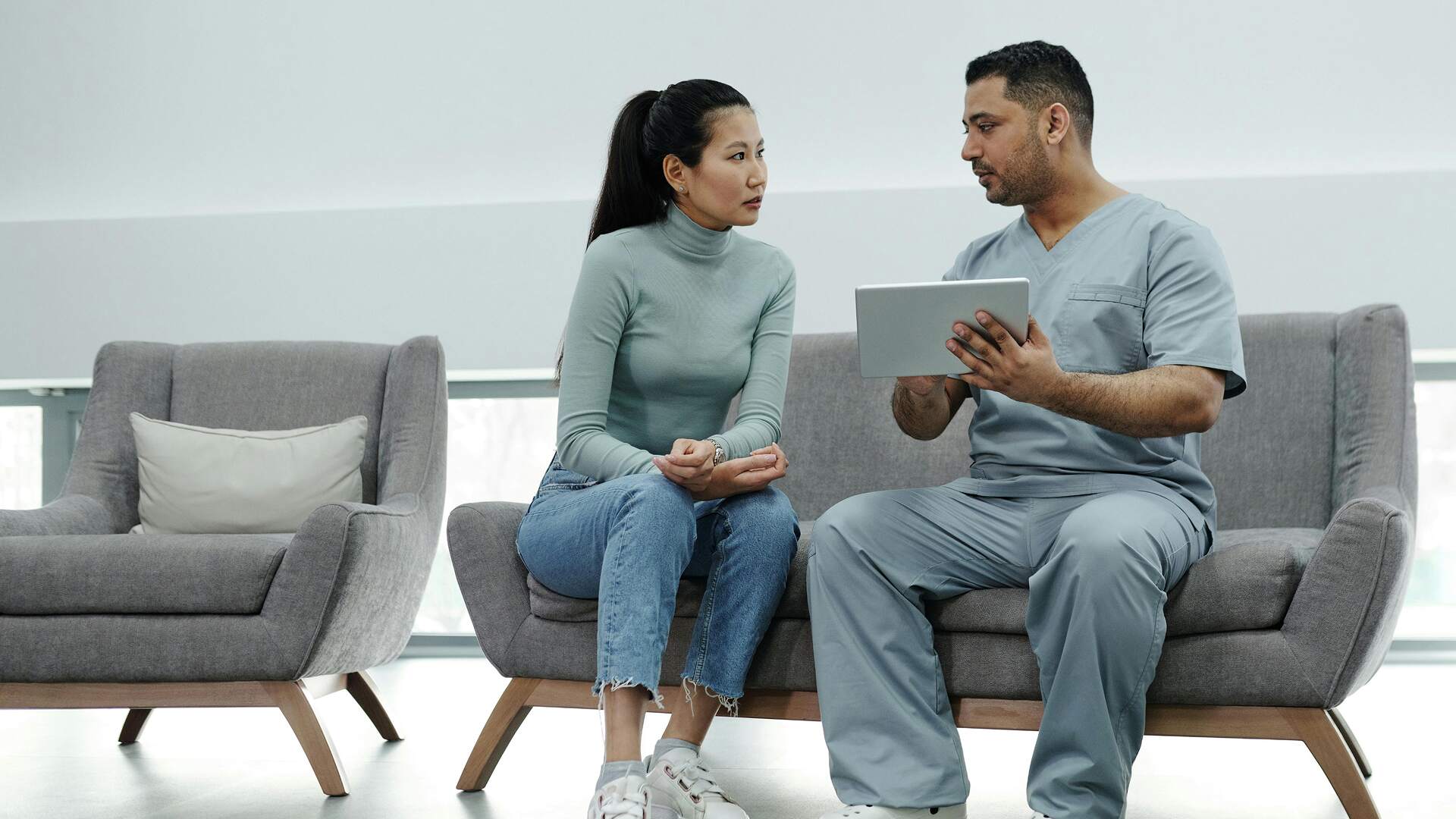 Healthcare professional discussing patient’s health information on tablet in clinic lounge.