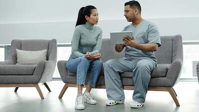 Healthcare professional discussing patient’s health information on tablet in clinic lounge.