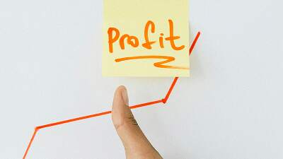 Hand pointing to a profit note with a red upward trend line representing business and revenue growth.