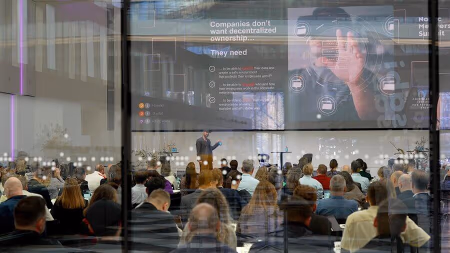Audience sitting in a modern conference room watching a speaker present with a large screen displaying text about companies and decentralized ownership.