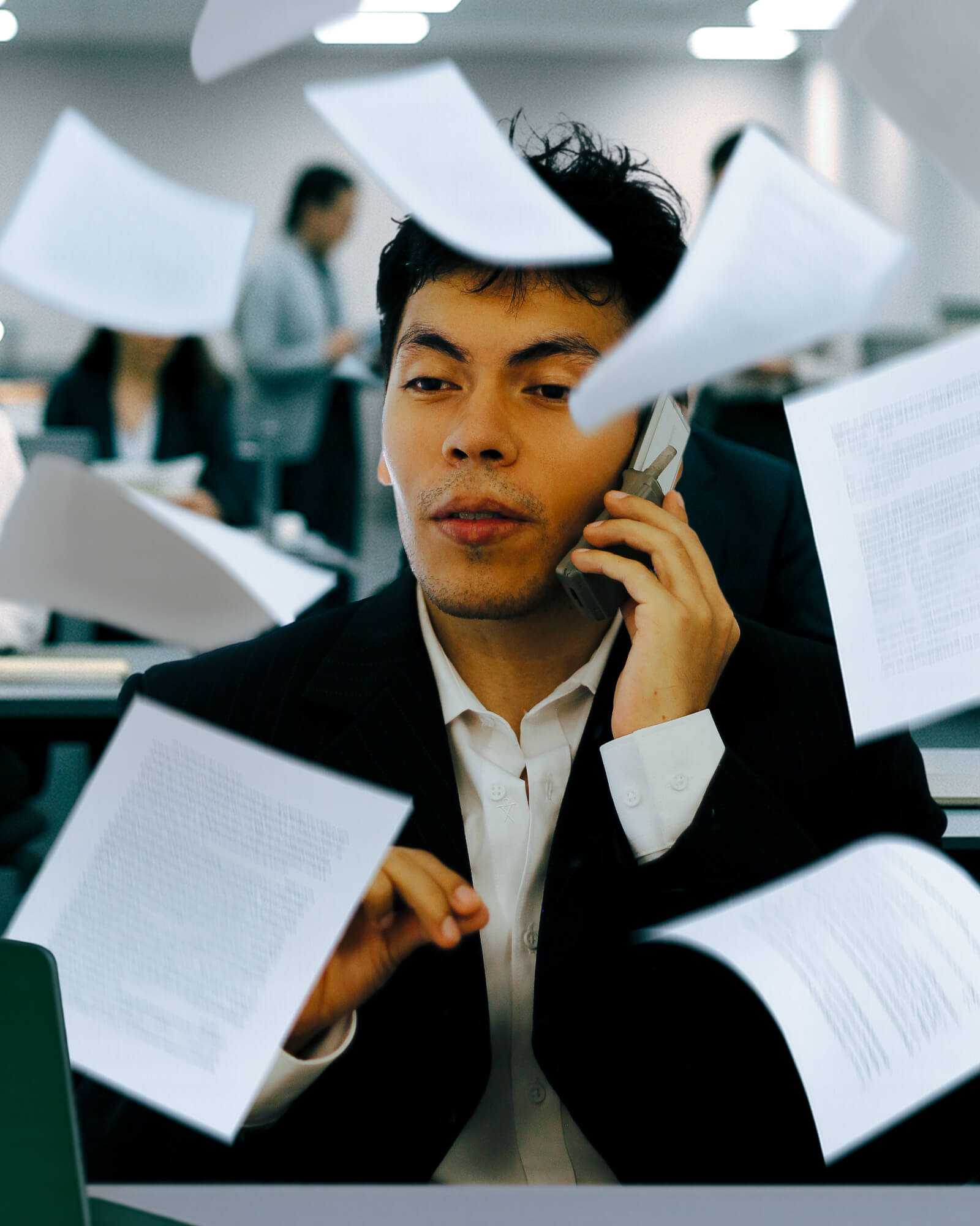Busy professional (Antonio Bautista) talking on the phone with documents flying around, symbolizing multitasking and workplace pressure.