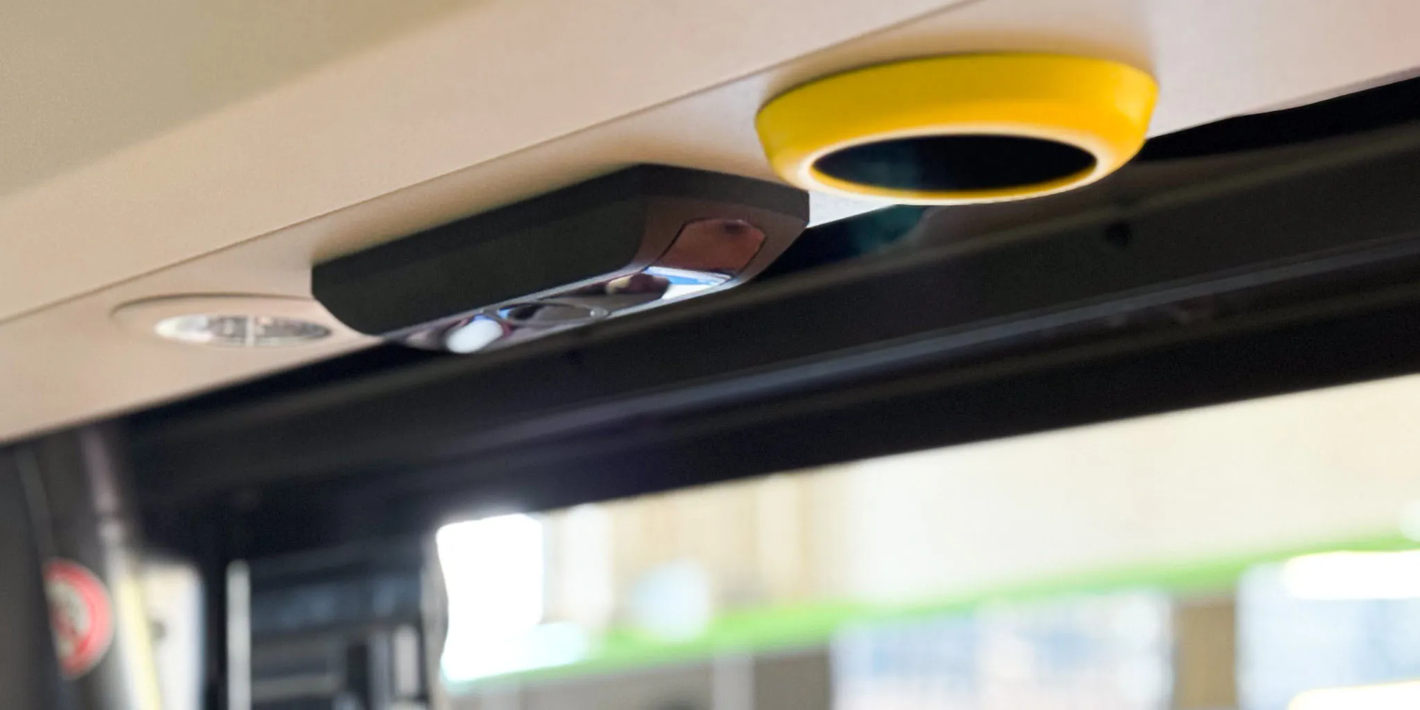 Close-up of a black and yellow sensor device mounted on the ceiling inside a vehicle.