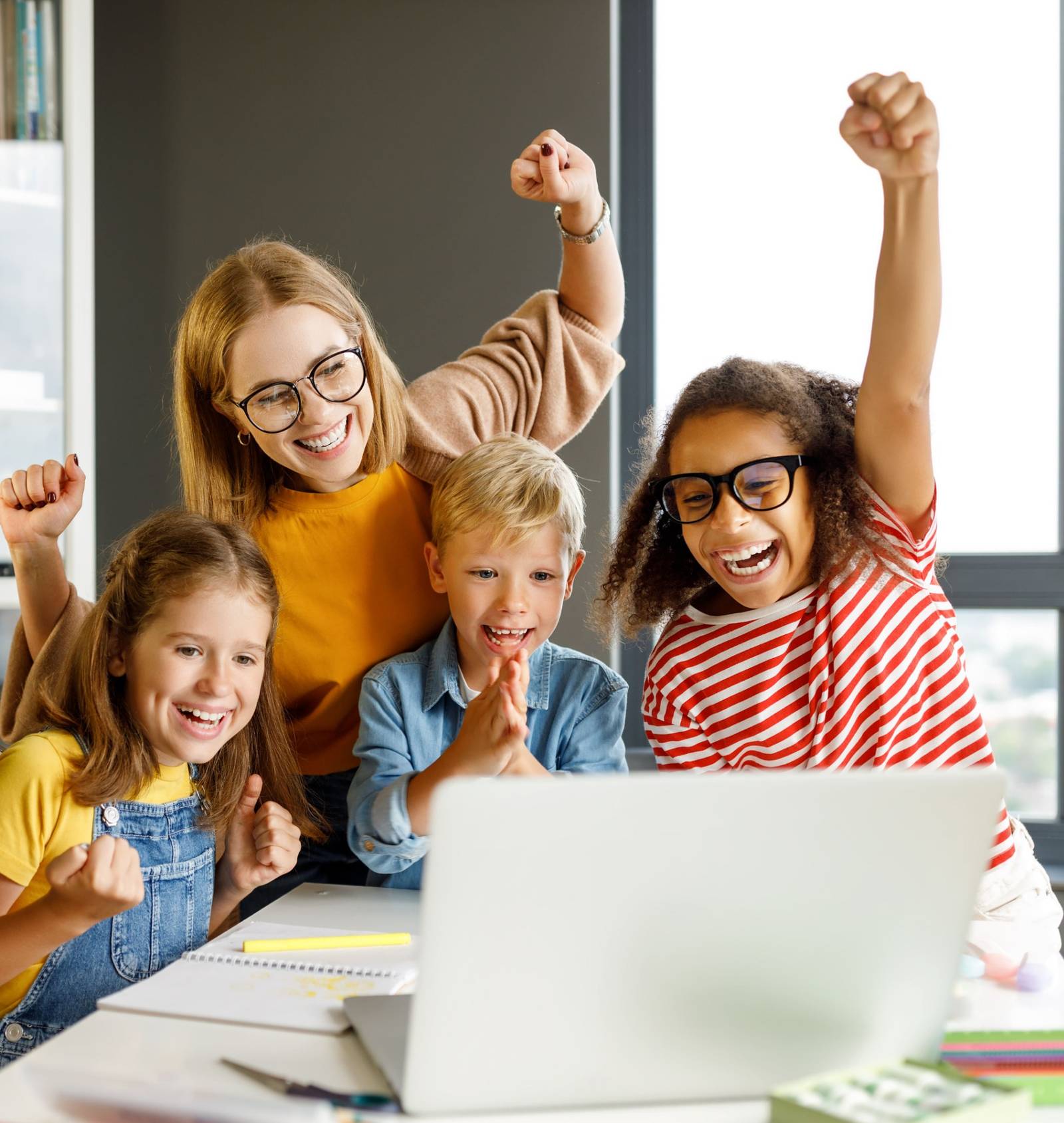 Lehrerin und Kinder jubeln gemeinsam vor einem Laptop