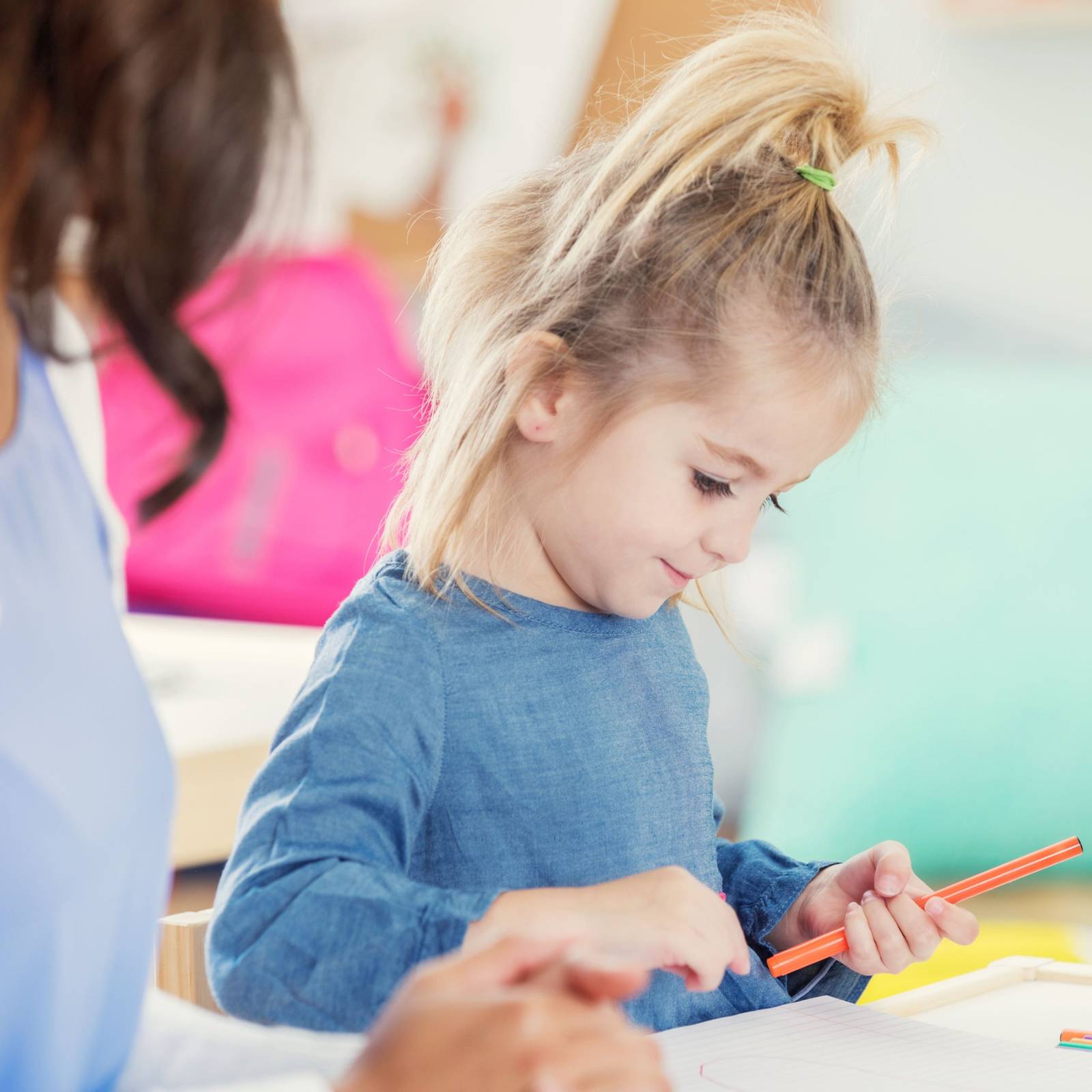 Kleines Mädchen malt konzentriert mit einem roten Stift im Unterricht