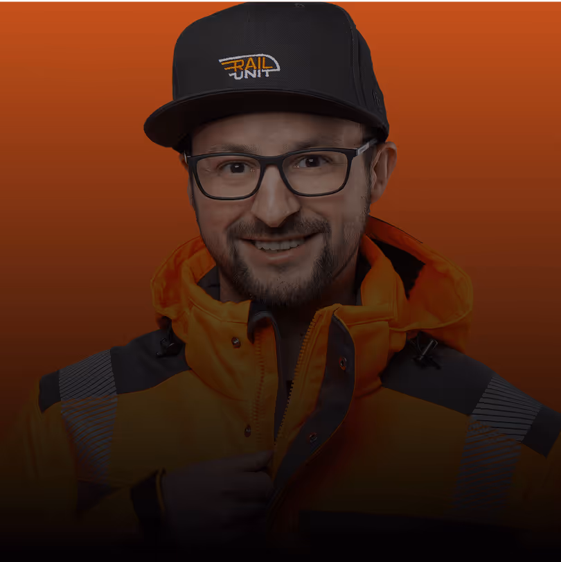 Mann mit Brille, schwarzer Cap und orangefarbener Jacke vor orangefarbenem Hintergrund.