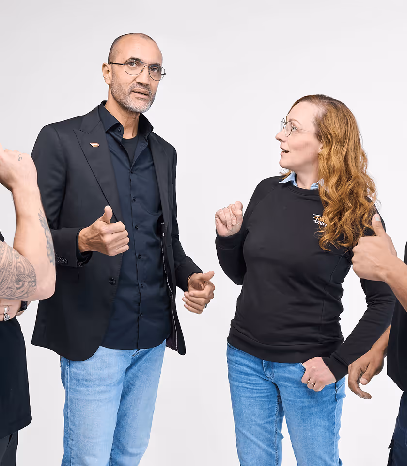 Vier Personen diskutieren lebhaft, tragen lässige Kleidung und gestikulieren mit den Händen vor weißem Hintergrund.