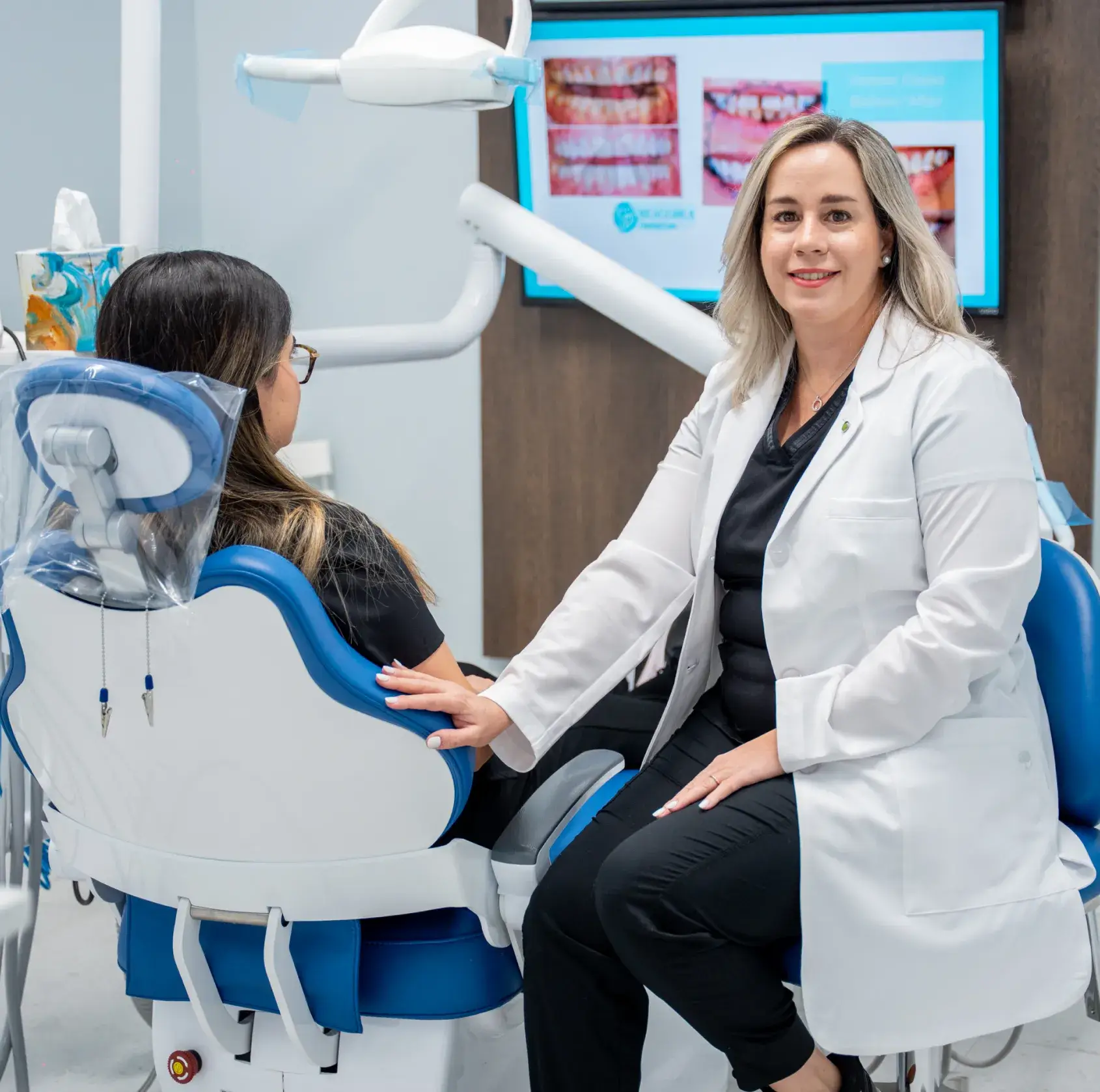A dentist hands a dental appliance to a seated patient in a clinic.