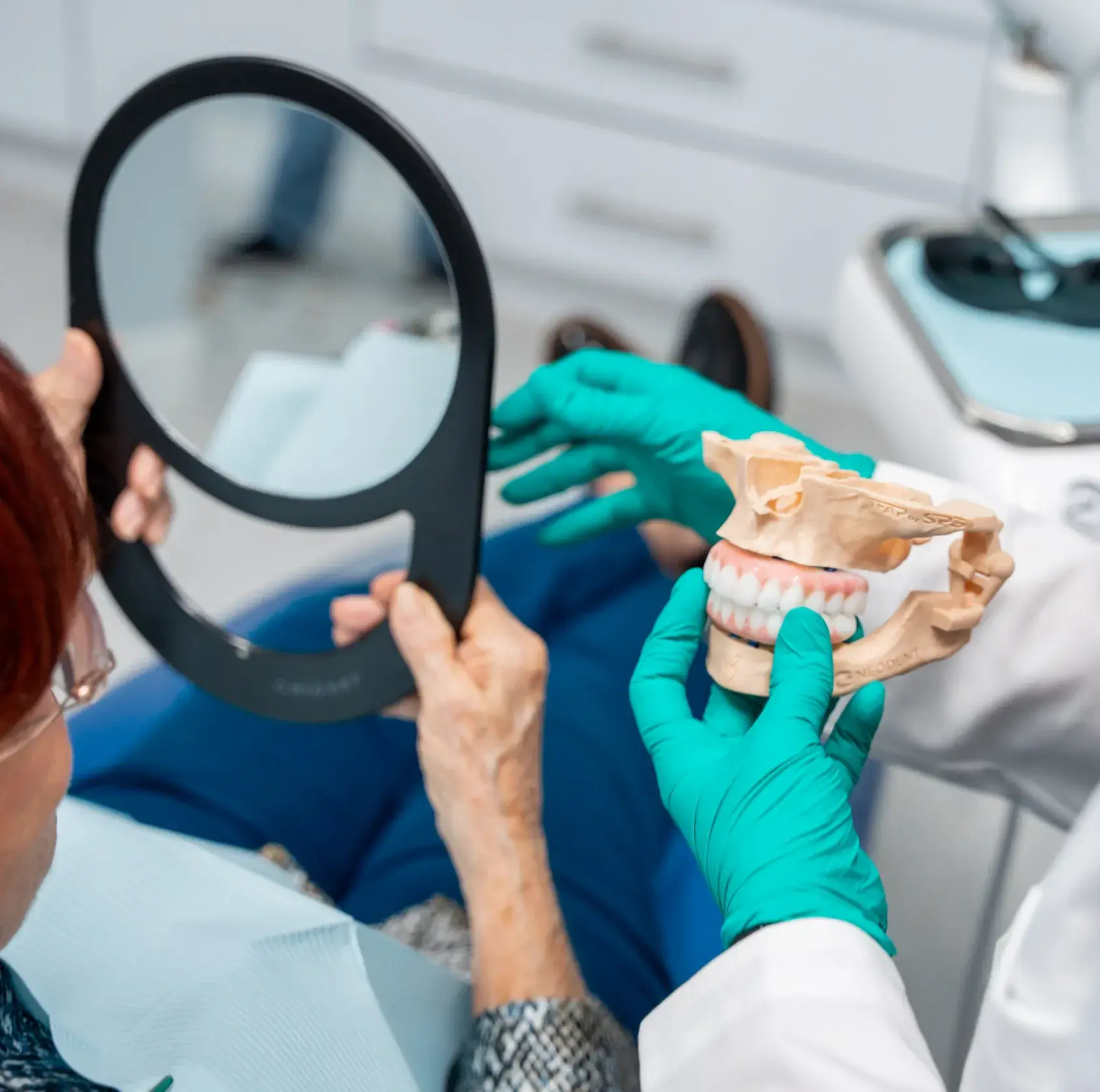 A person with curly hair smiles while standing against a plain, light-colored background.