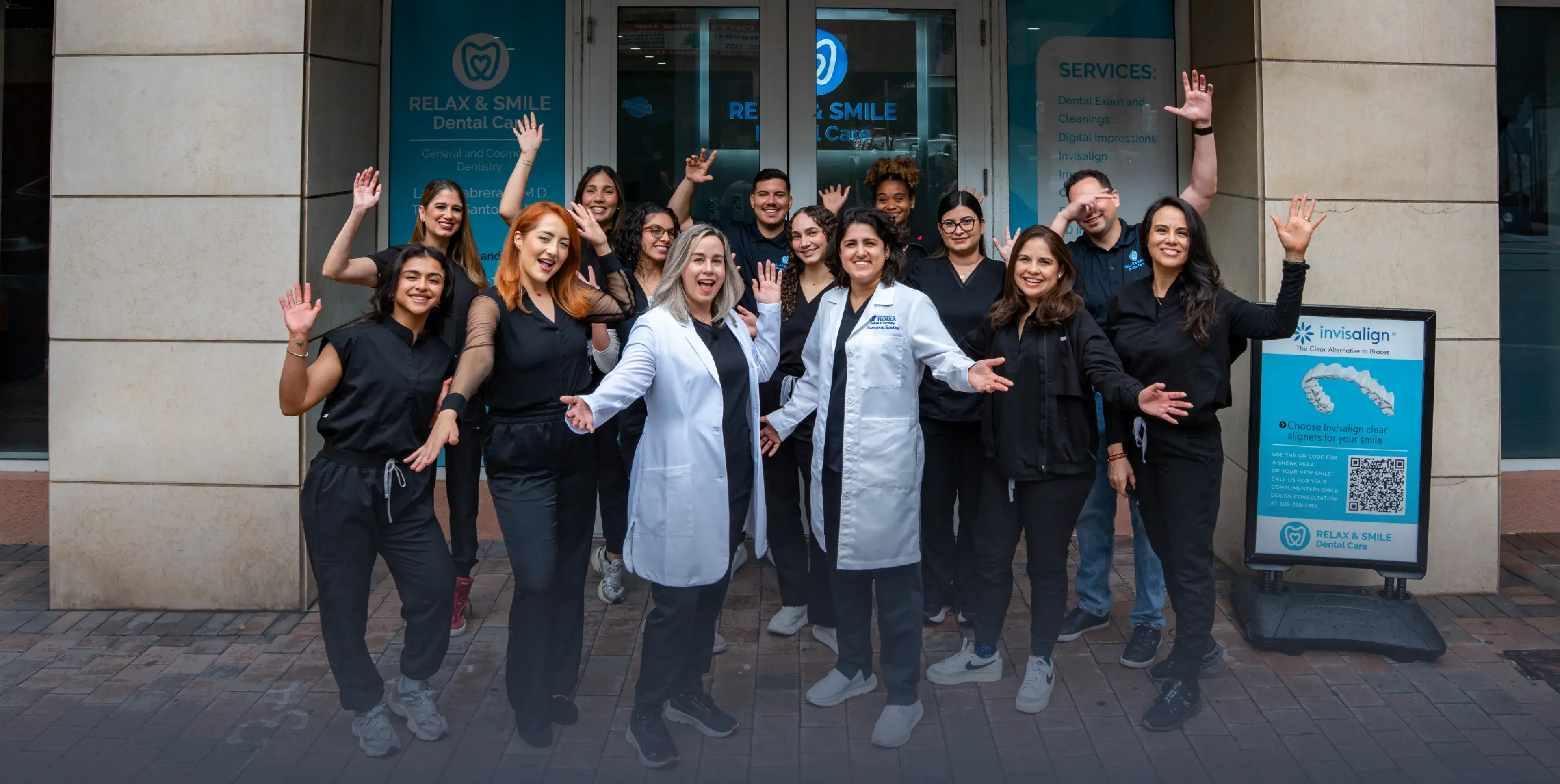 Smiling dental care team standing outside their clinic waving at the camera.