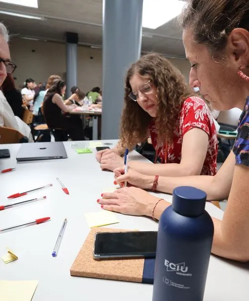 ECIU participants collaborating at workshop table with branded university water bottle