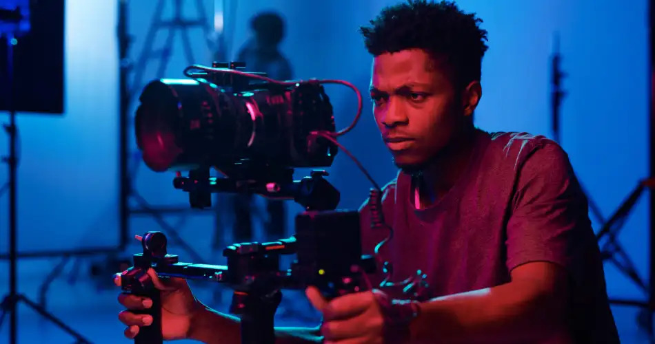 Étudiant en formation cinéma utilisant un stabilisateur gimbal pour filmer avec une caméra professionnelle en studio.