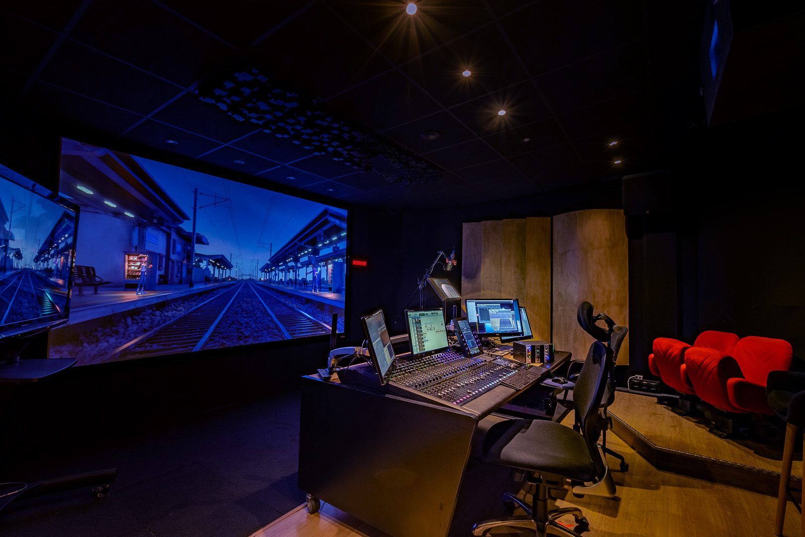 Studio de post-production cinéma avec console de mixage audio, écrans et salle de projection.