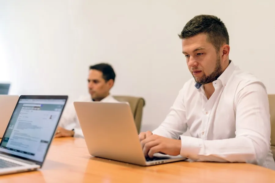 Office work: participants sit at a table with open laptops, neutral background.
